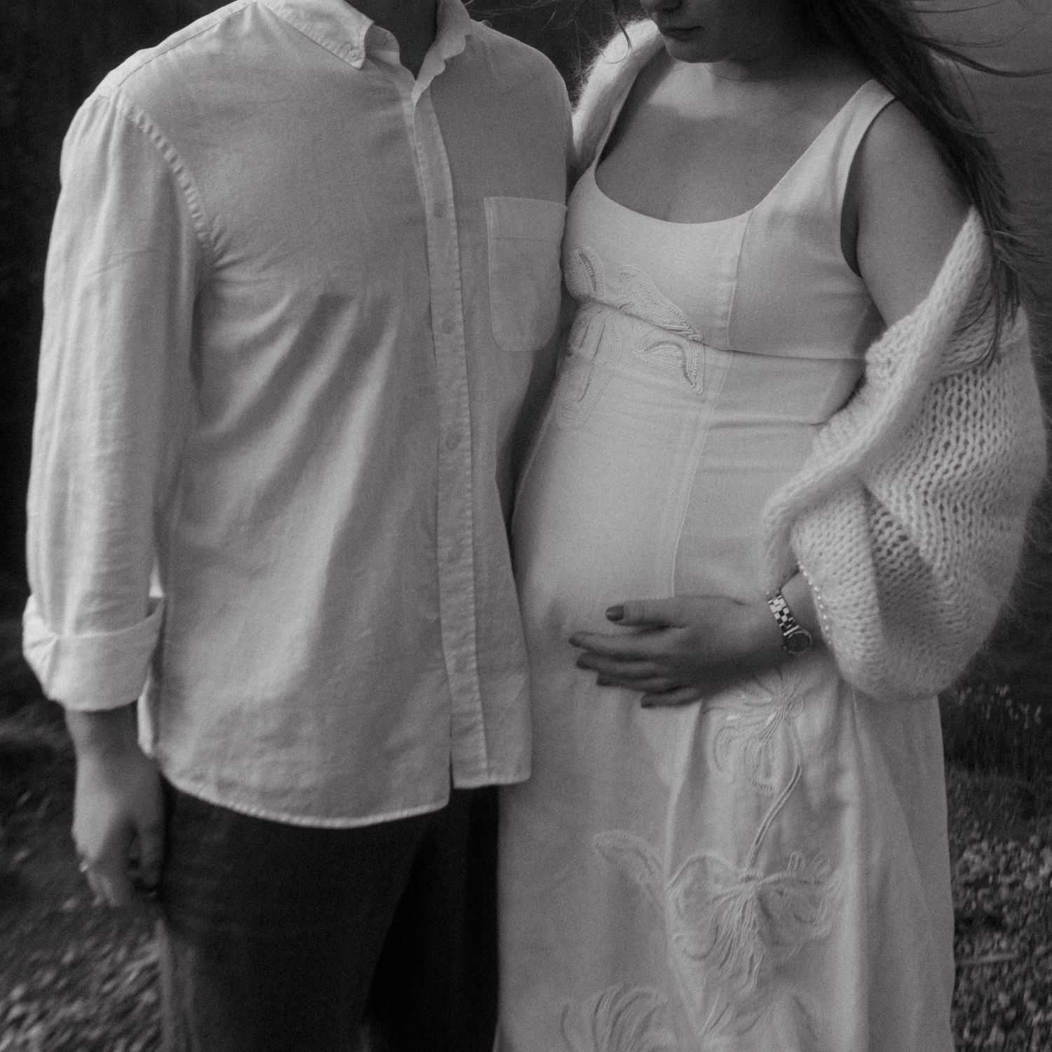 Black and white photograph of a couple, framed to not show their faces. She's holding her pregnant belly.