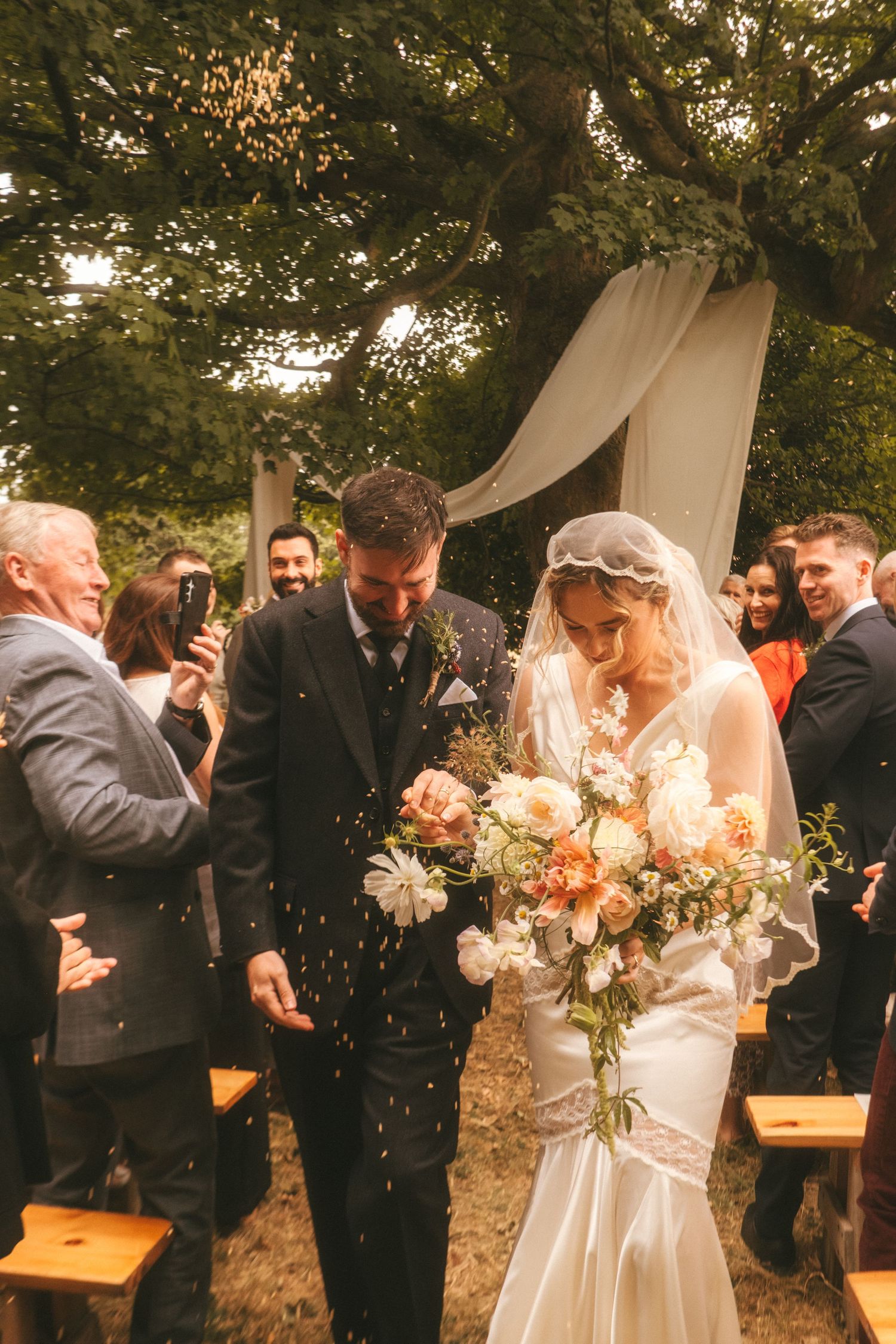 Photograph of bride and groom exiting their ceremony, barley is being thrown at them in celebration