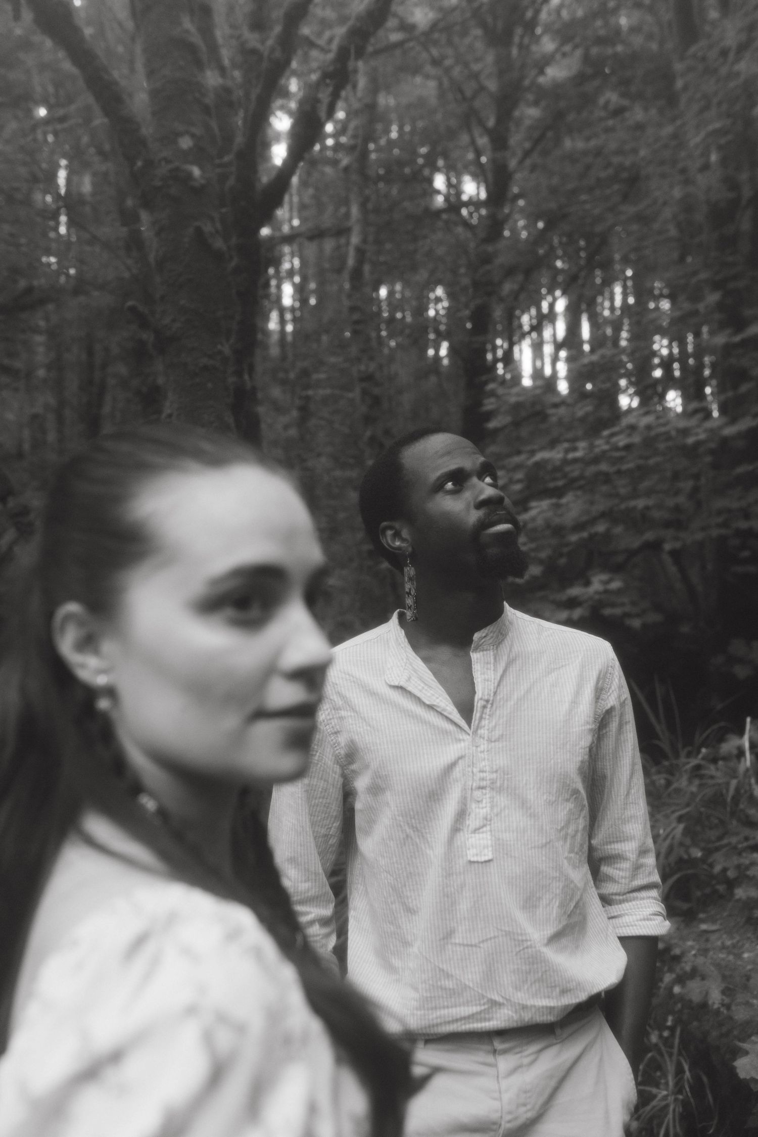 Black and white photograph of an interracial couple, she's out of focus in the foreground, while he is standing behind