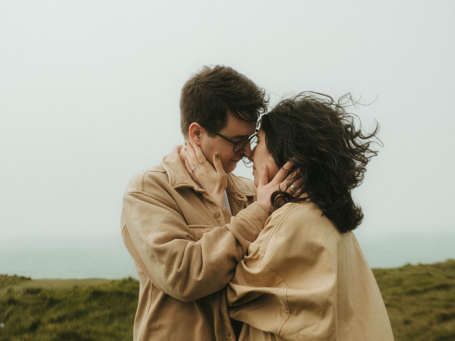 Photograph of couple about to kiss, her hair is blowing in the wind.
