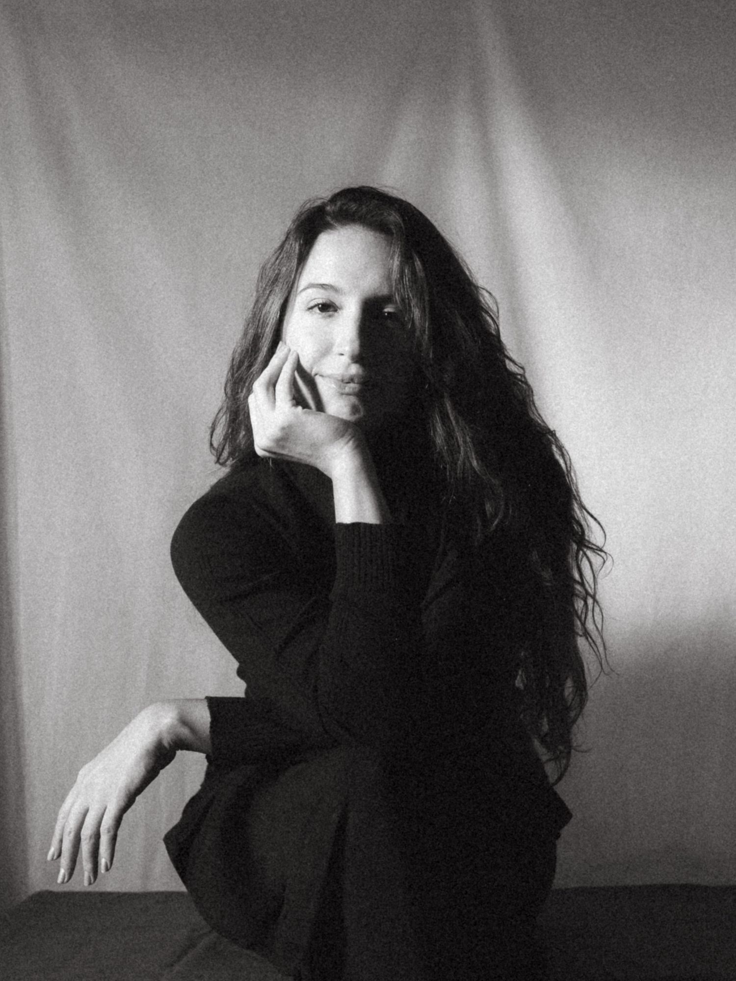 Black and white photograph of a dark haired model in a studio setting, soft contrast.