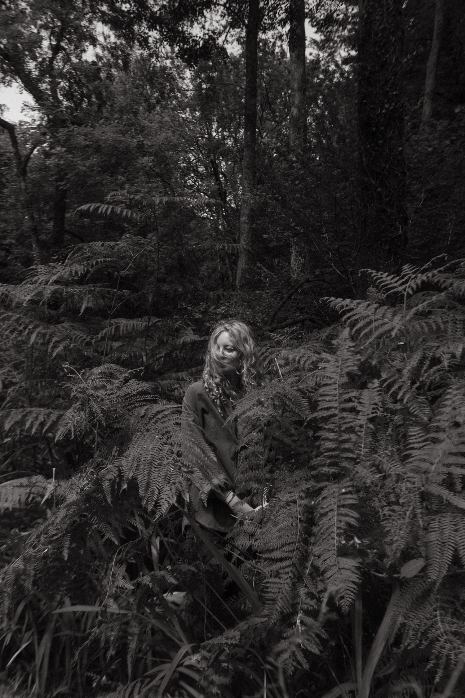 Black and white photo of Jacky Galm Photography standing in between ferns.