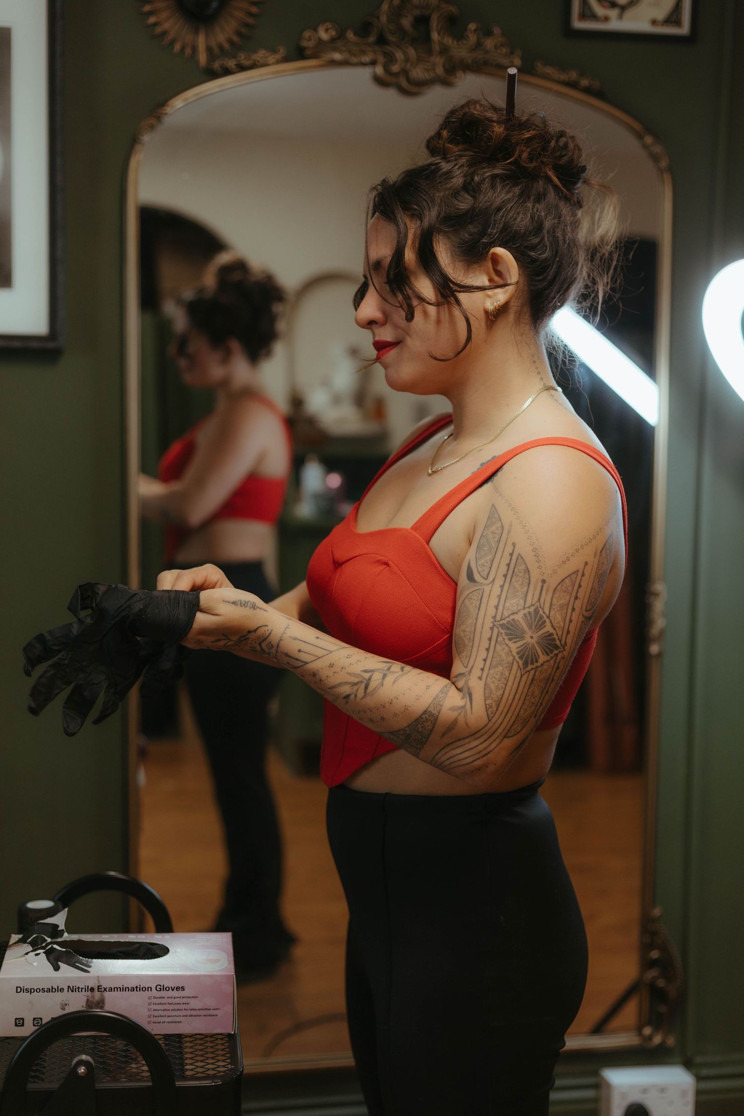 Photo of tattoo artist tattooing a client, she has her hair tied up and is wearing a red top