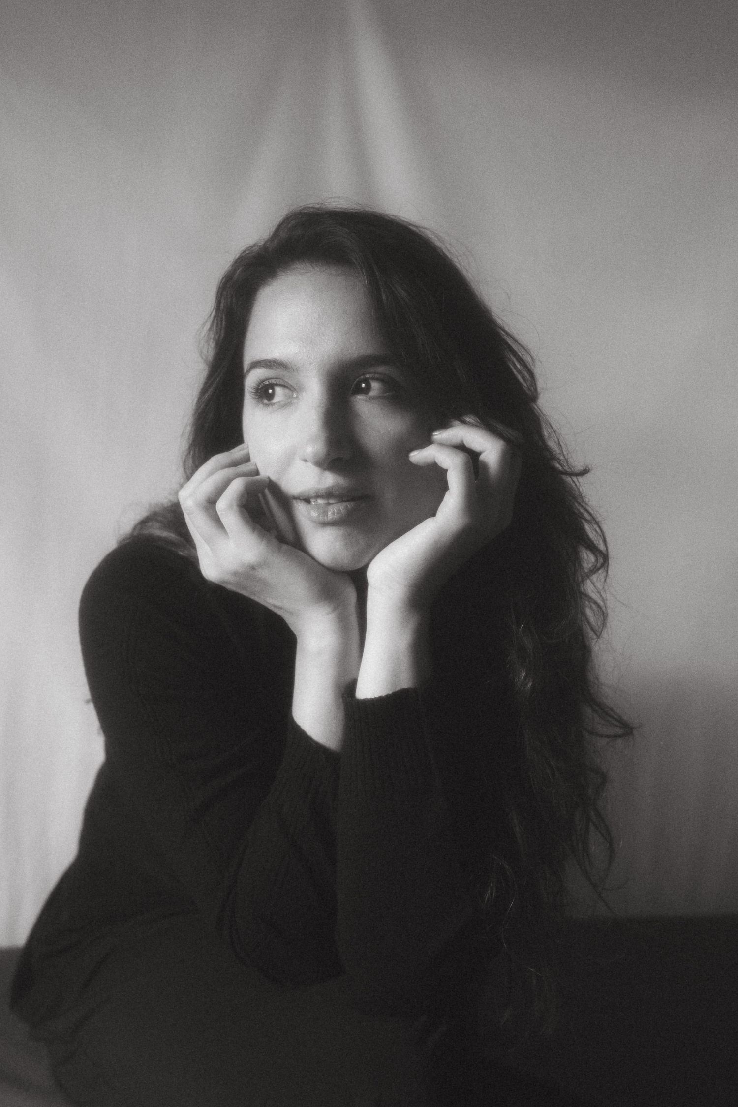 Black and white photograph of a dark haired model in a studio setting, soft contrast.