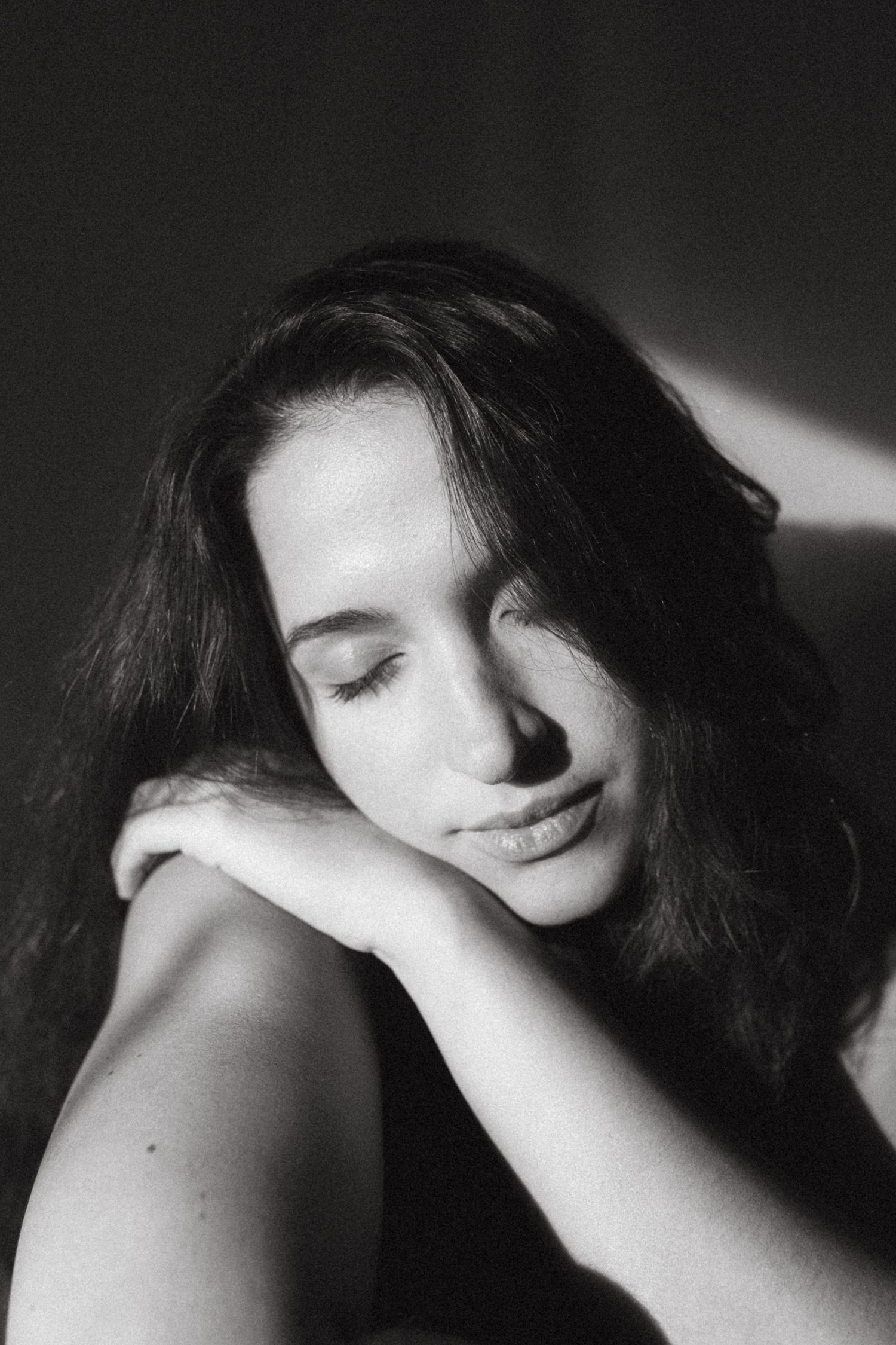 Black and white photograph of a dark haired model in a studio setting, soft contrast.