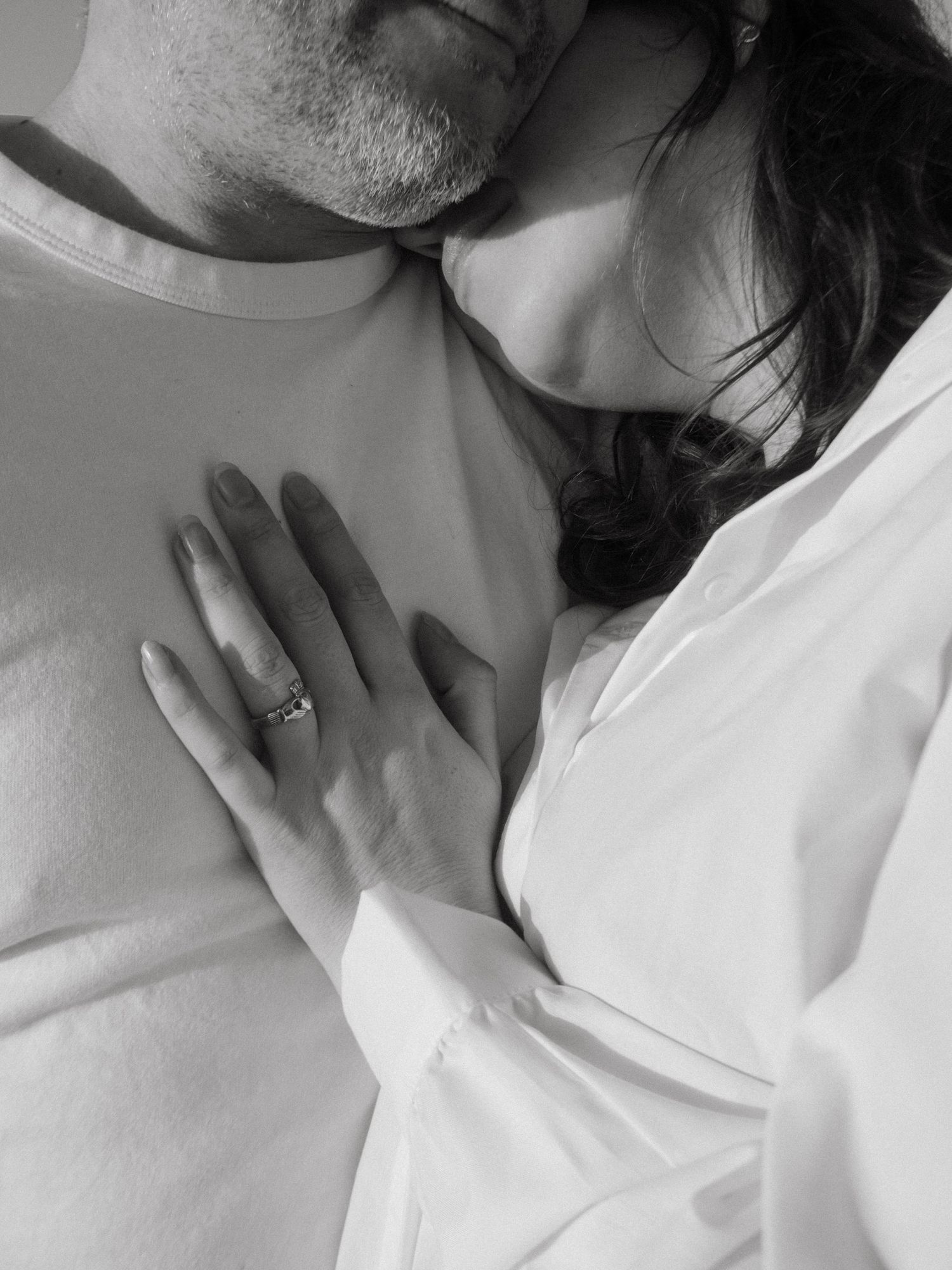 Black and white photo of a couple, she's leaning on his shoulder, the focus is on her hand on his chest, soft shadows