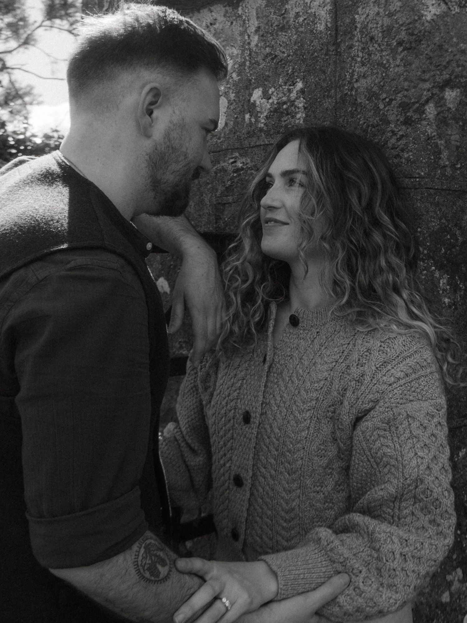 Black and white photo of a couple, she's leaning against a wall and he's gently gazing at her