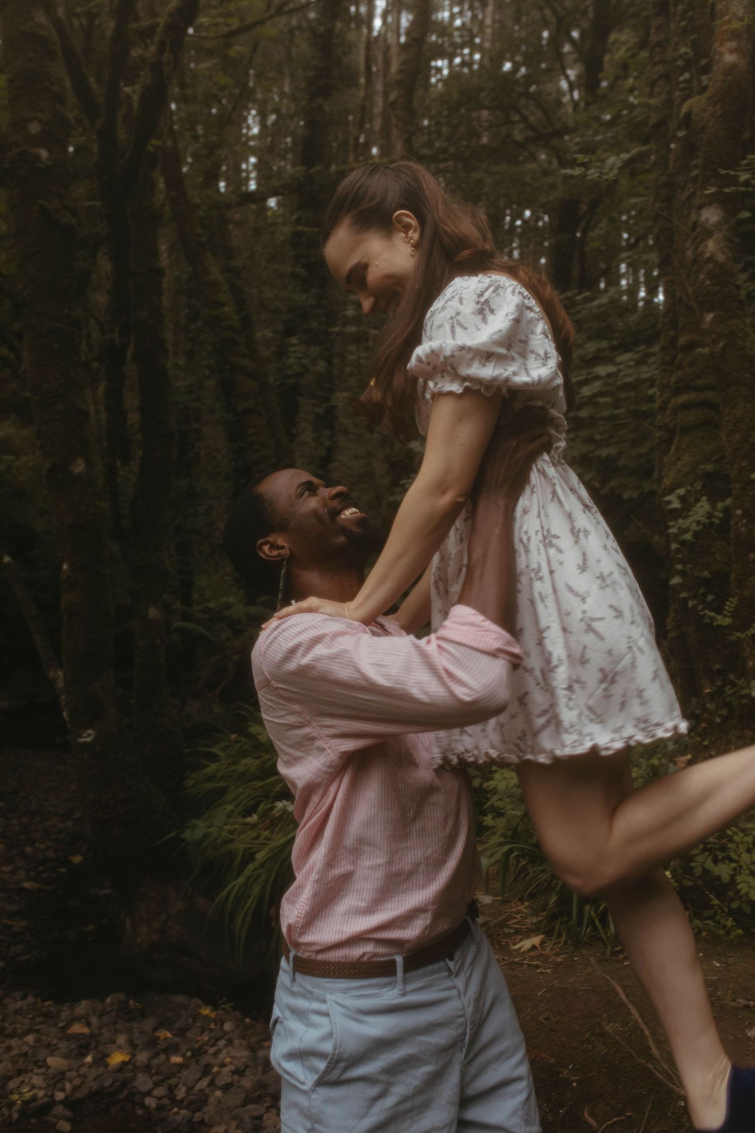Photograph of a couple in a forest, he is lifting her up by her waist