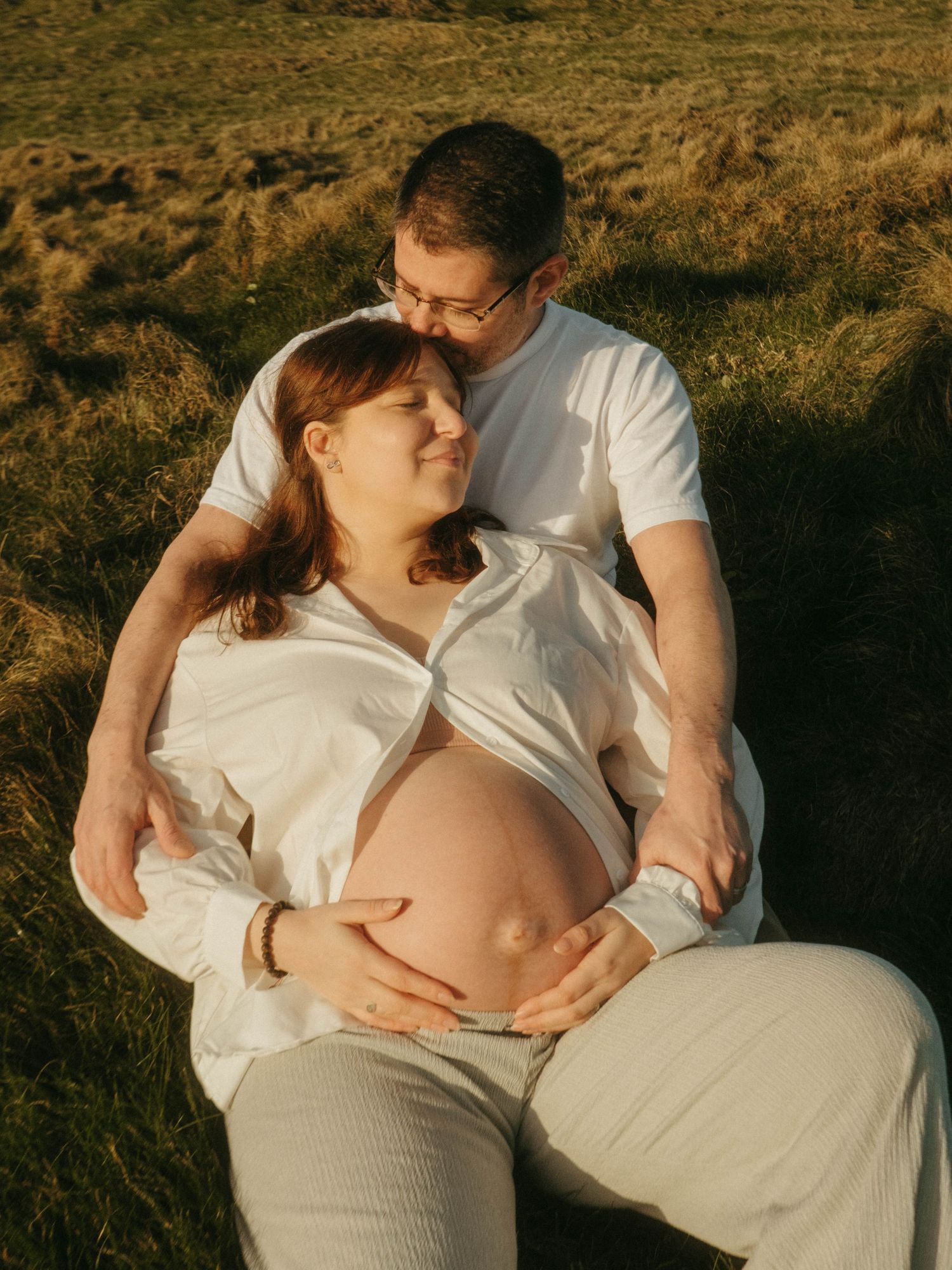 Photograph of a couple on a cliff outlooking the sea, she's leaning against him, they are sitting