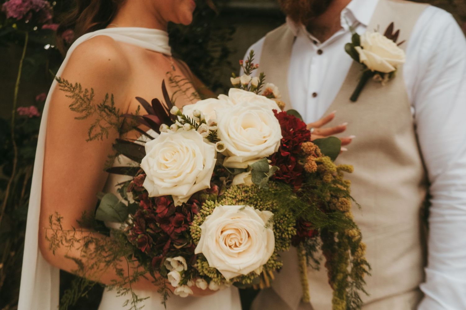 Photograph of bride and groom in a meadow after their wedding ceremony, she has dark brown hair and he is bald with a ginger beard.