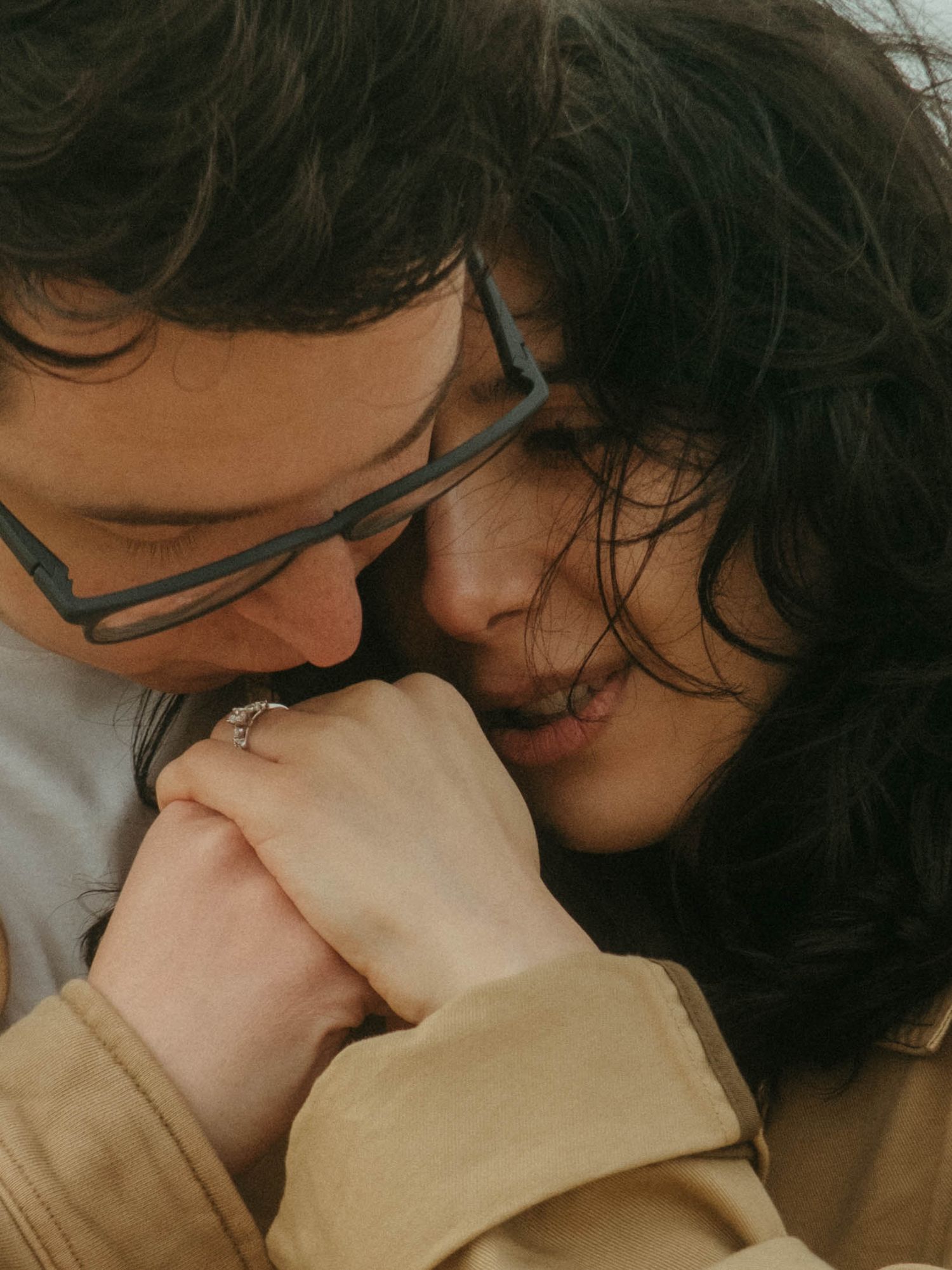Close up photograph of couple in wind, he is kissing her hand