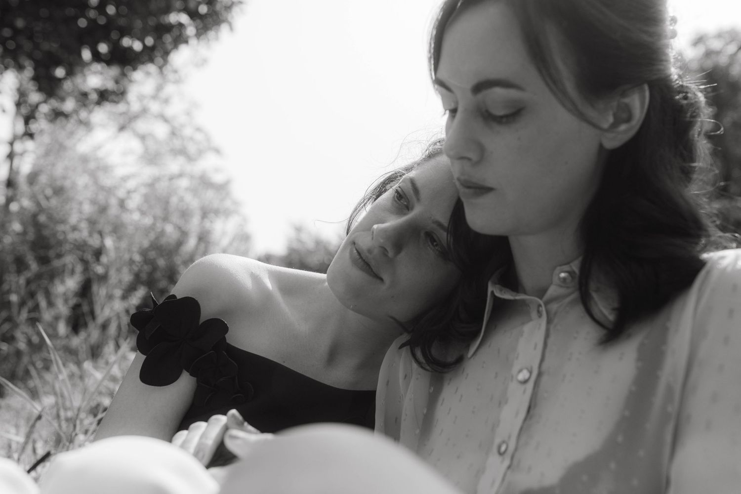 Black and white photograph of two brides after their civic ceremony, in a park, one of them is leaning on the others shoulder.