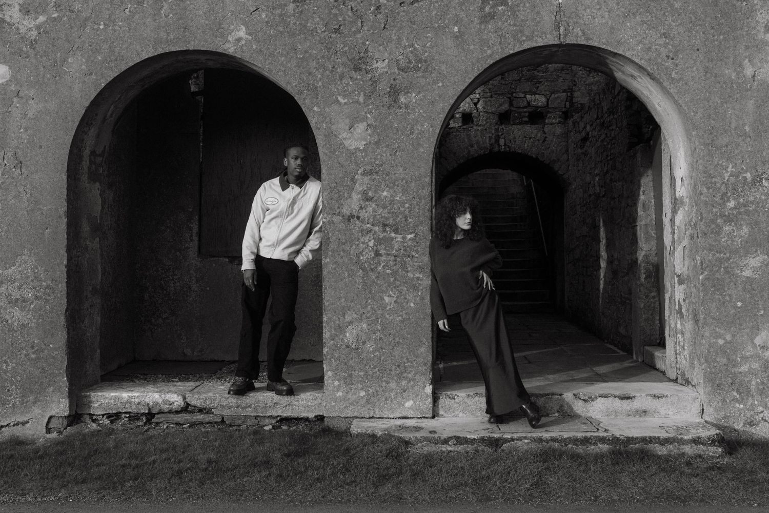 Black and white photograph of couple both standing in a rounded doorway leaning against the wall