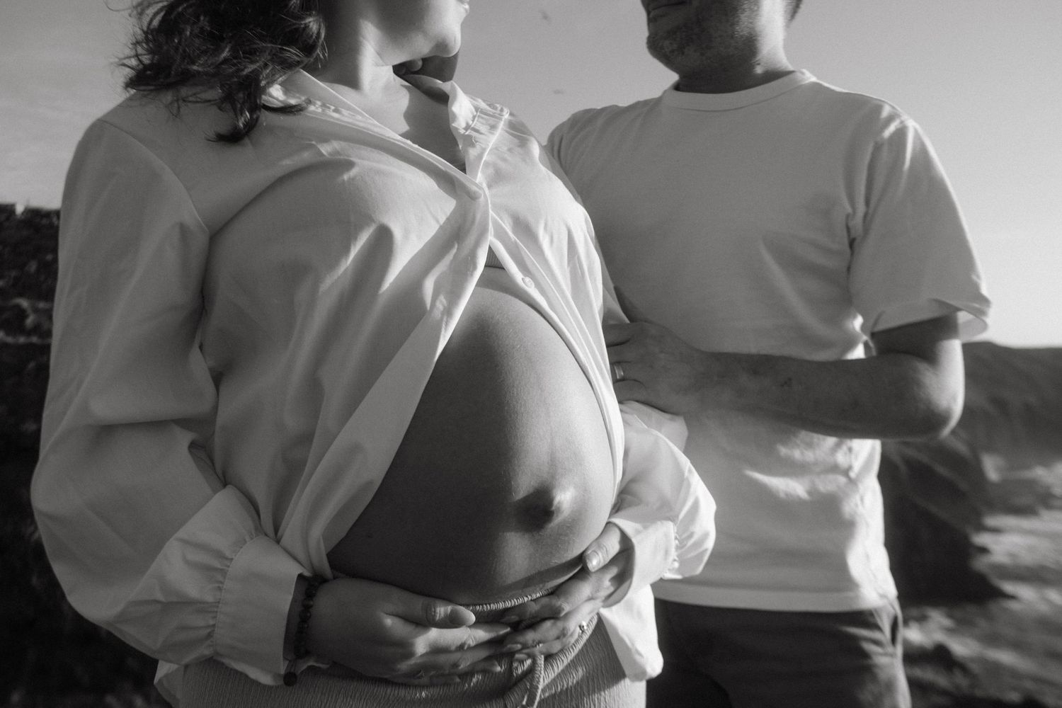 Black and white photograph of a couple, she's in front the focus is on her pregnant belly, he's in the background