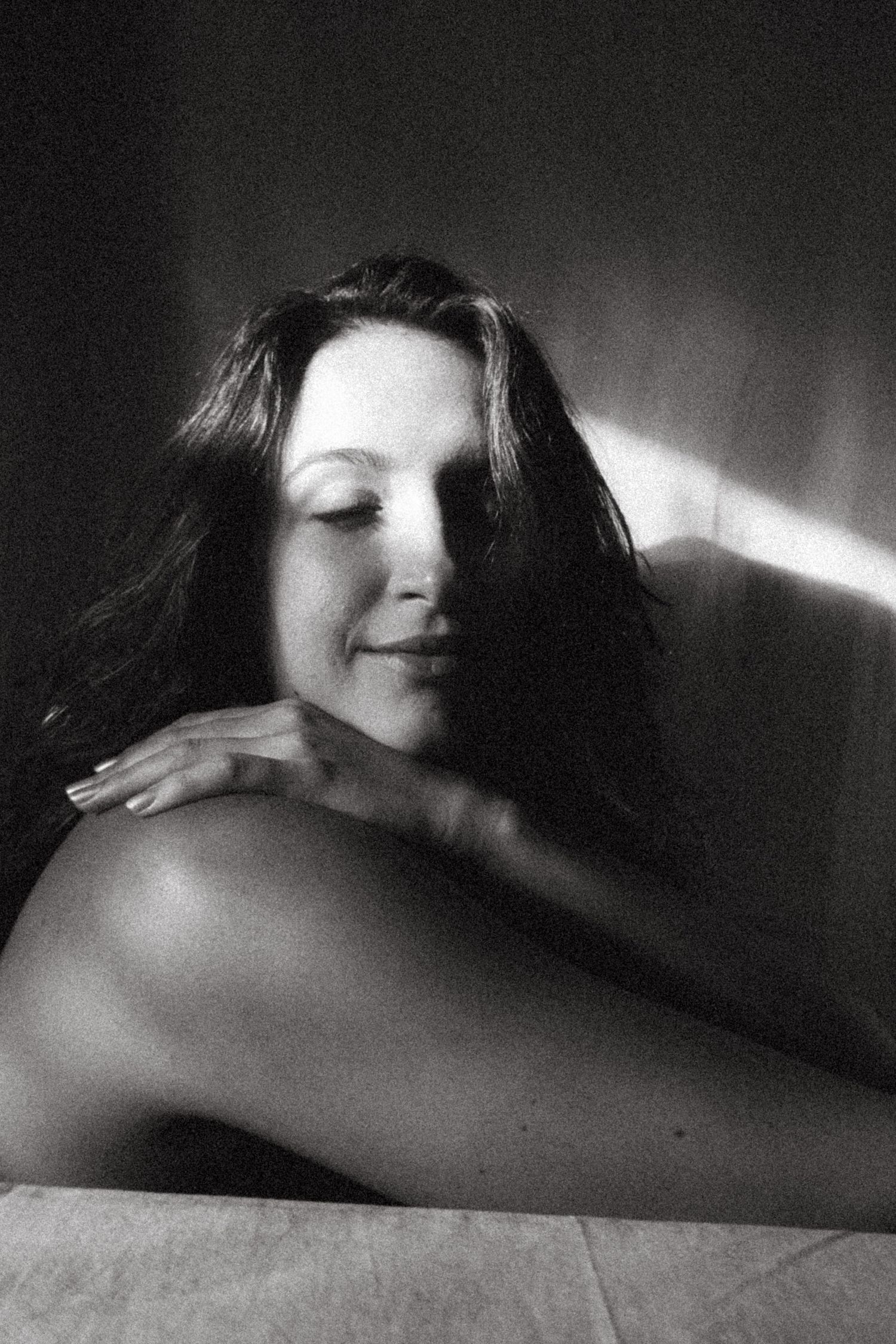 Black and white photograph of a dark haired model in a studio setting, soft contrast.
