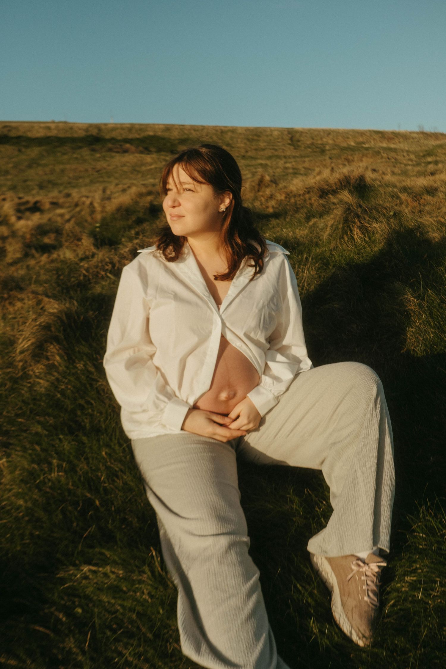 Photograph of pregnant woman sitting in a field, direct sun is shining on her
