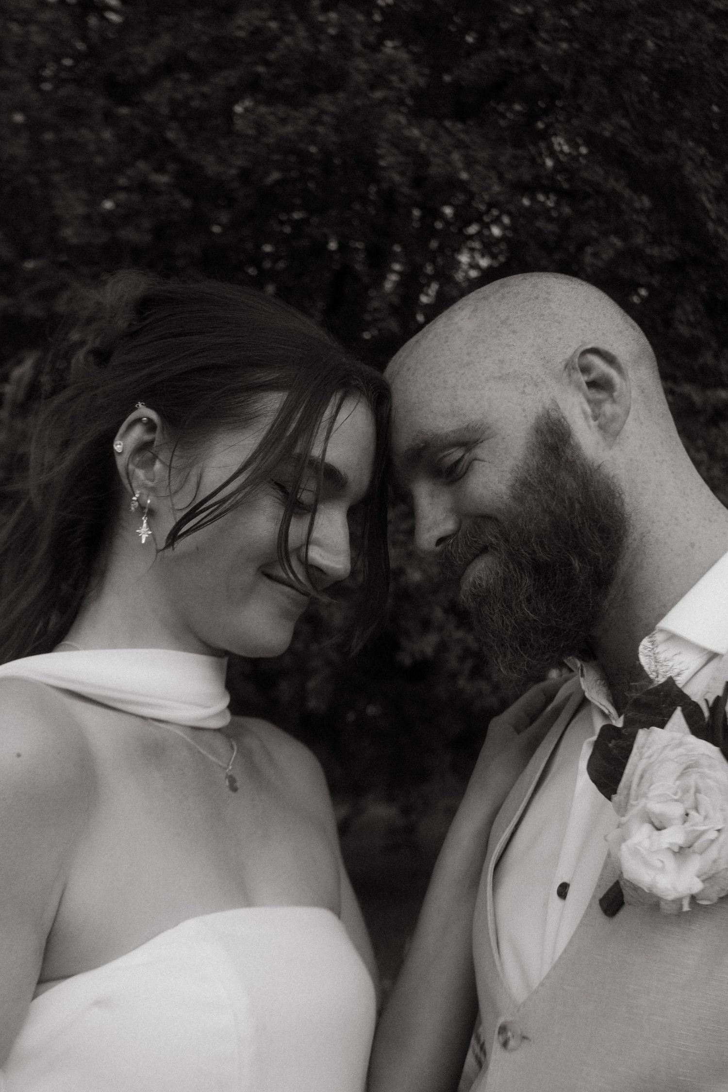Photograph of bride and groom, she has dark brown hair and he is bald with a ginger beard.
