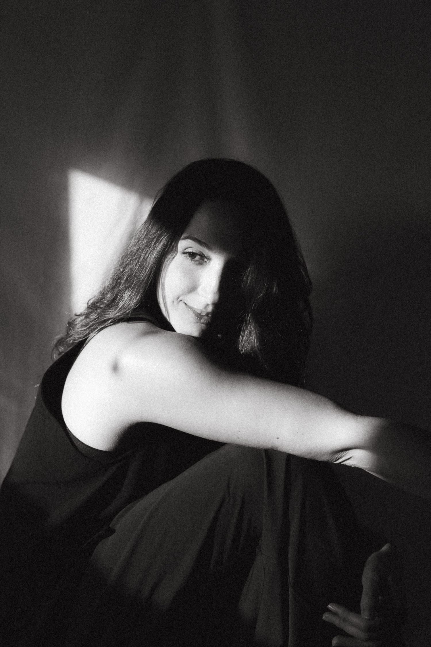 Black and white photograph of a dark haired model in a studio setting, soft contrast.