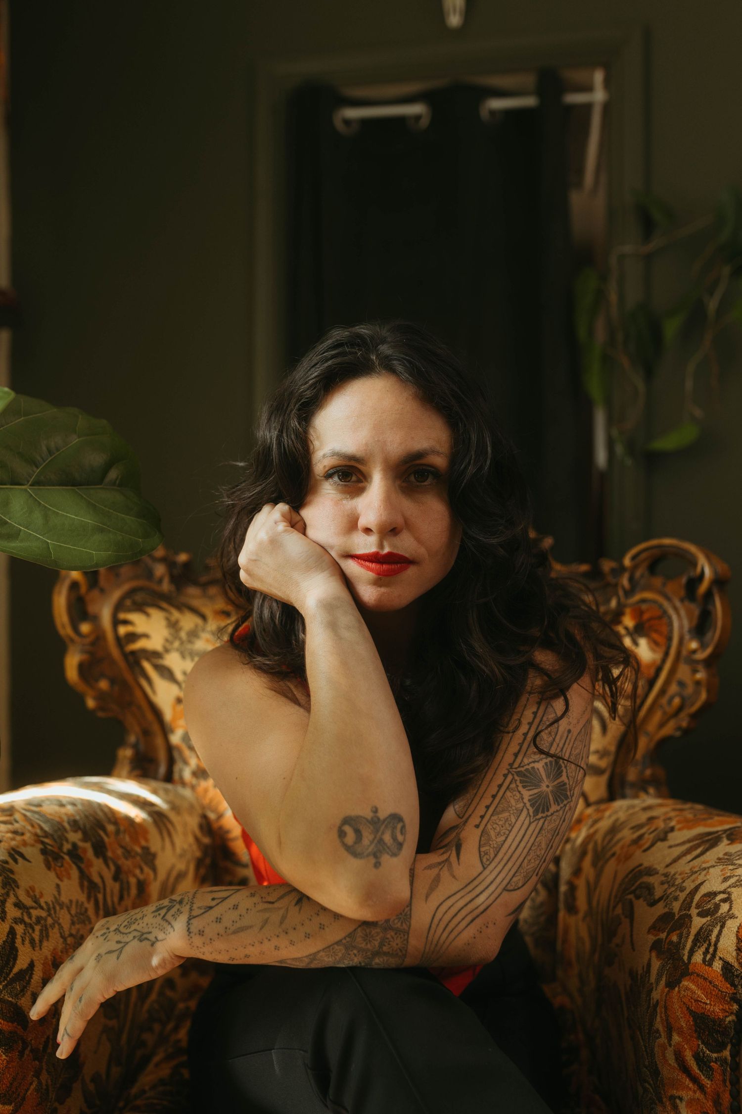 Portrait of woman leaning her chin against her hand looking to the left, dark hair and tattoos