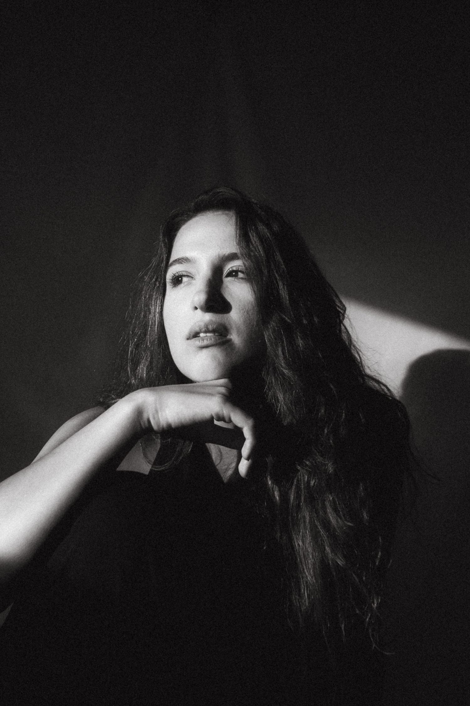 Black and white portrait photograph of young woman with dark hair, the sun is illuminating her face from the left