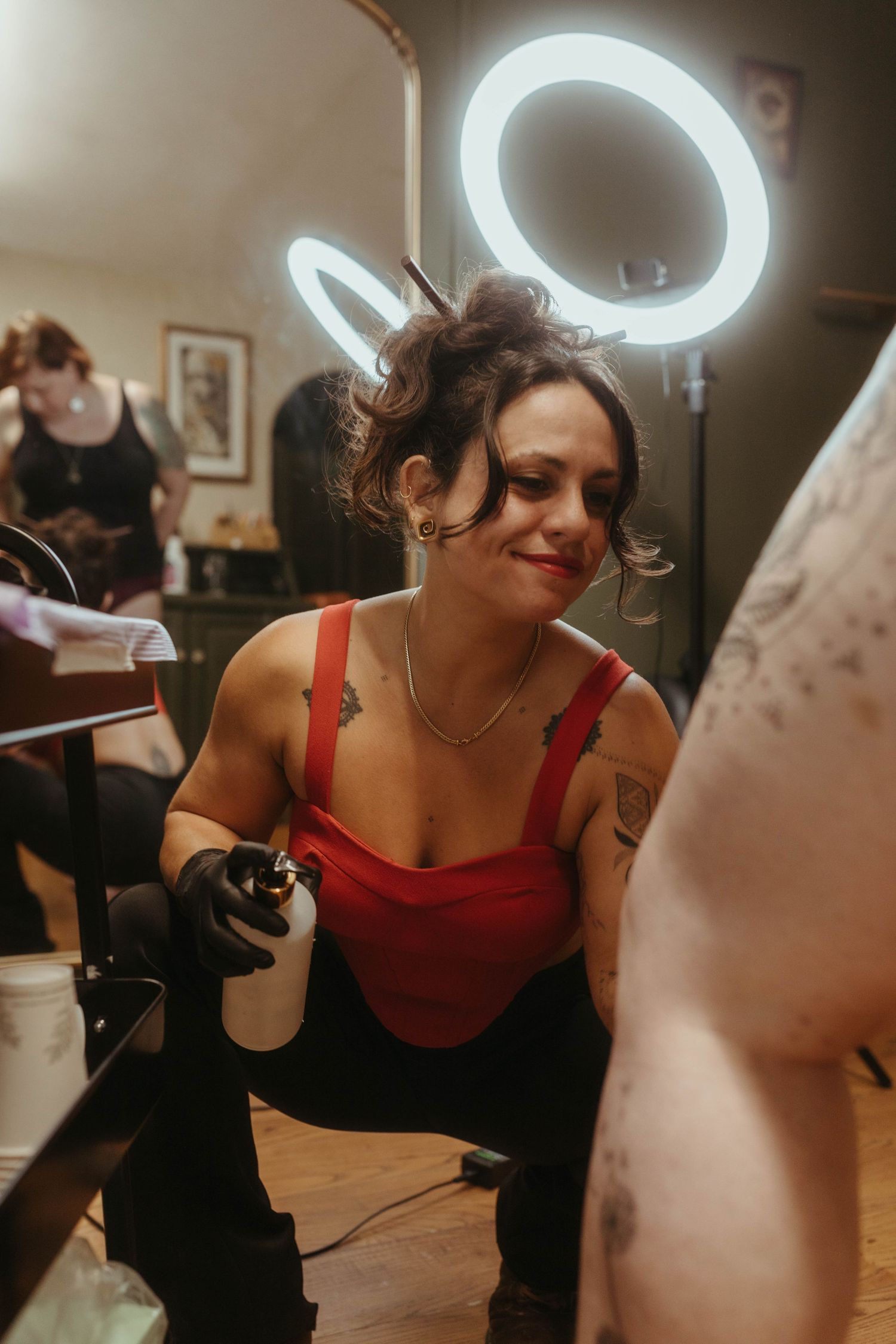 Photo of tattoo artist tattooing a client, she has her hair tied up and is wearing a red top