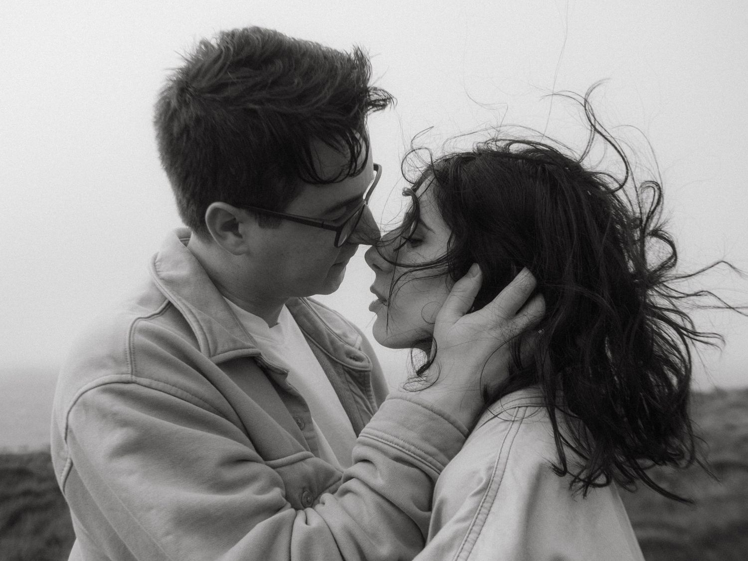 Black and white Photograph of a couple in windy conditions, he's holding her face.
