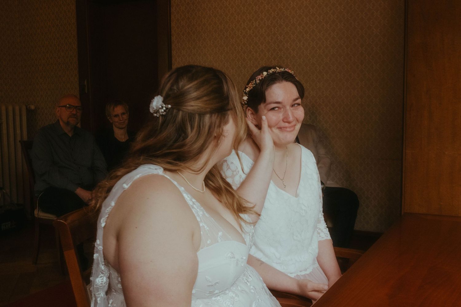 Photograoh of two brides at their civic wedding, one of them is stroking the others cheek, her eyes are filled with happy tears.