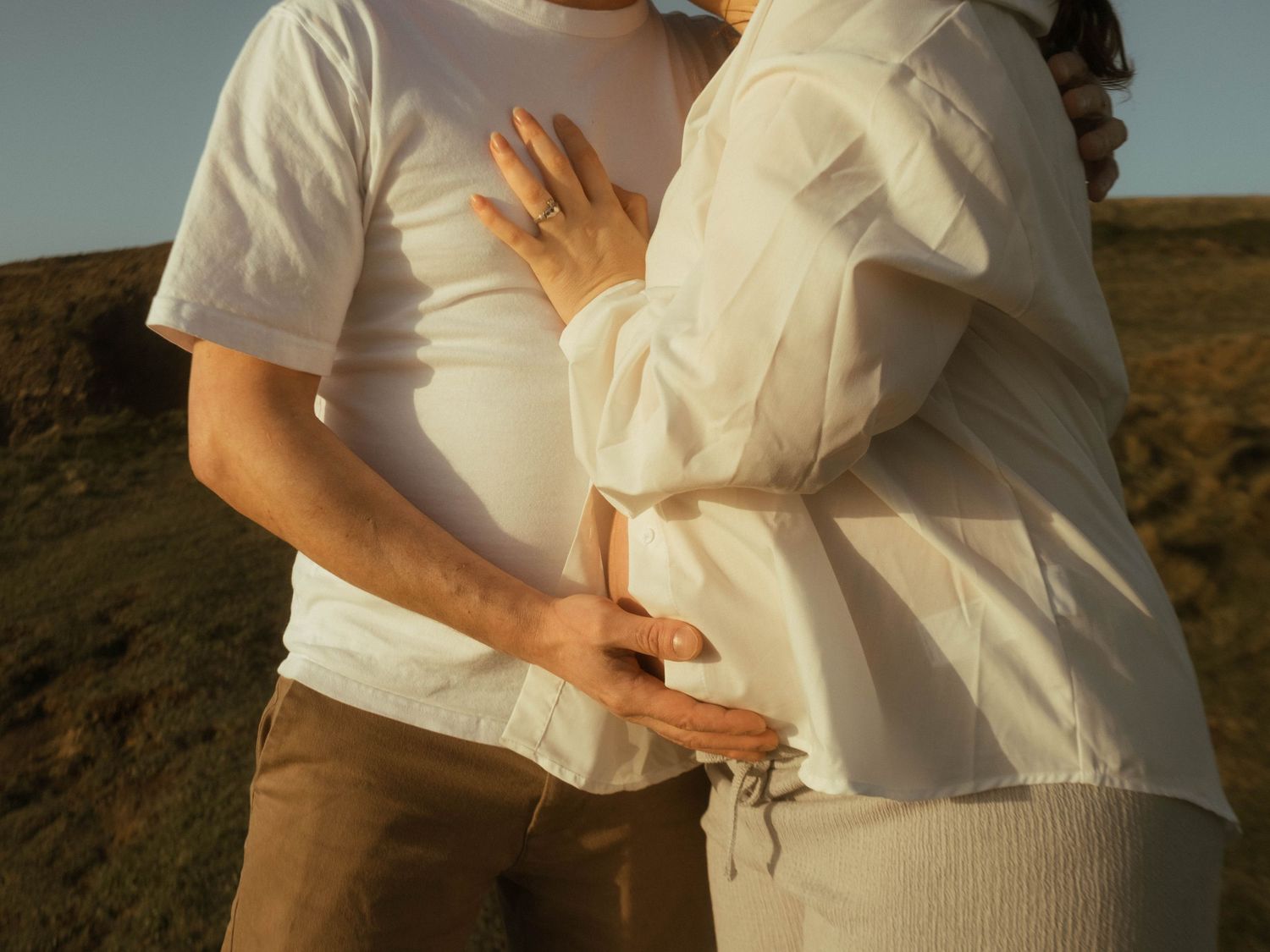 Photograph of a couple embracing each other, he's supporting her baby belly.