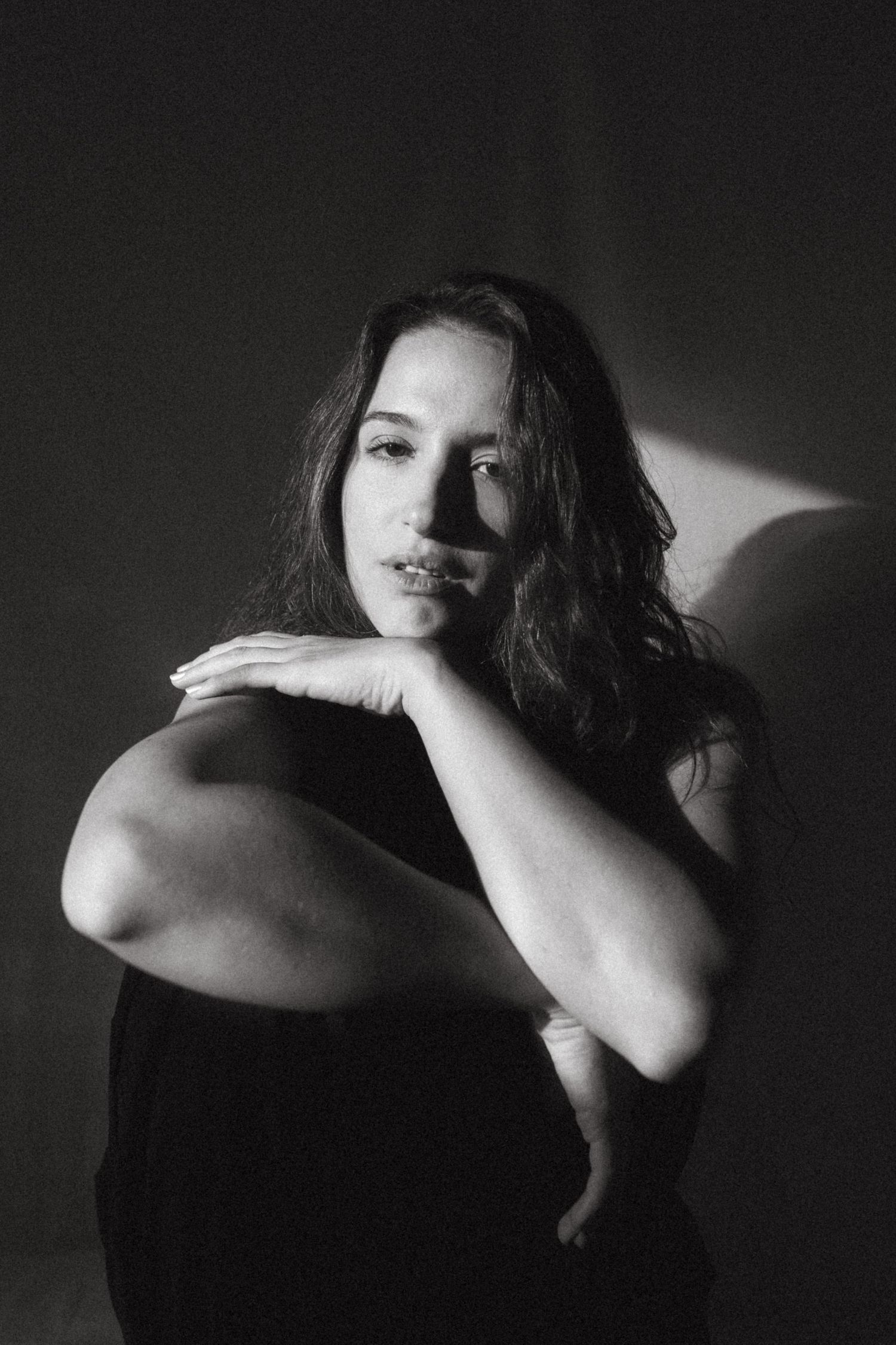 Black and white photograph of a dark haired model in a studio setting, soft contrast.