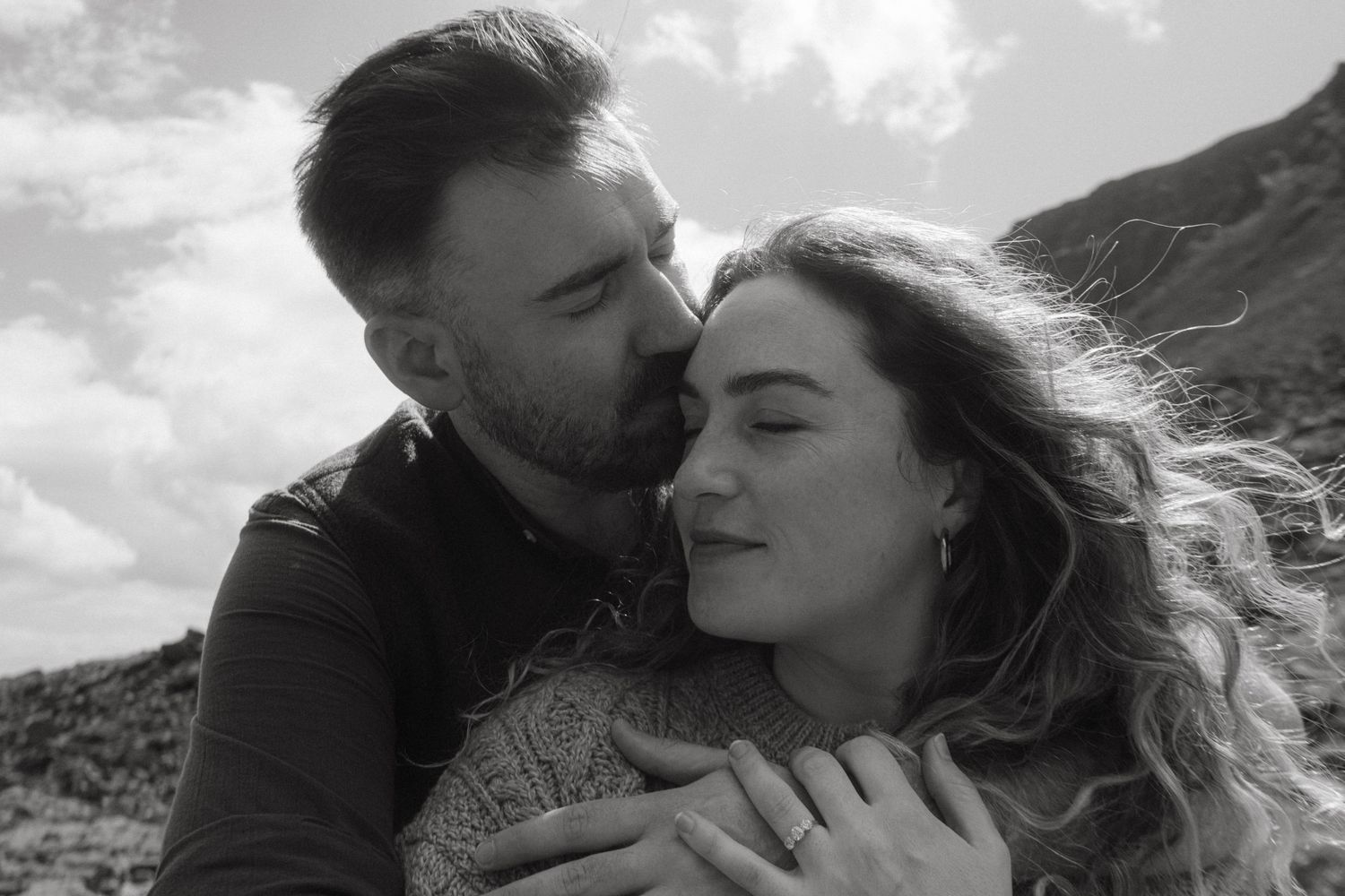 Photograph of couple, the wind is blowing her hair, he's kissing her forehead
