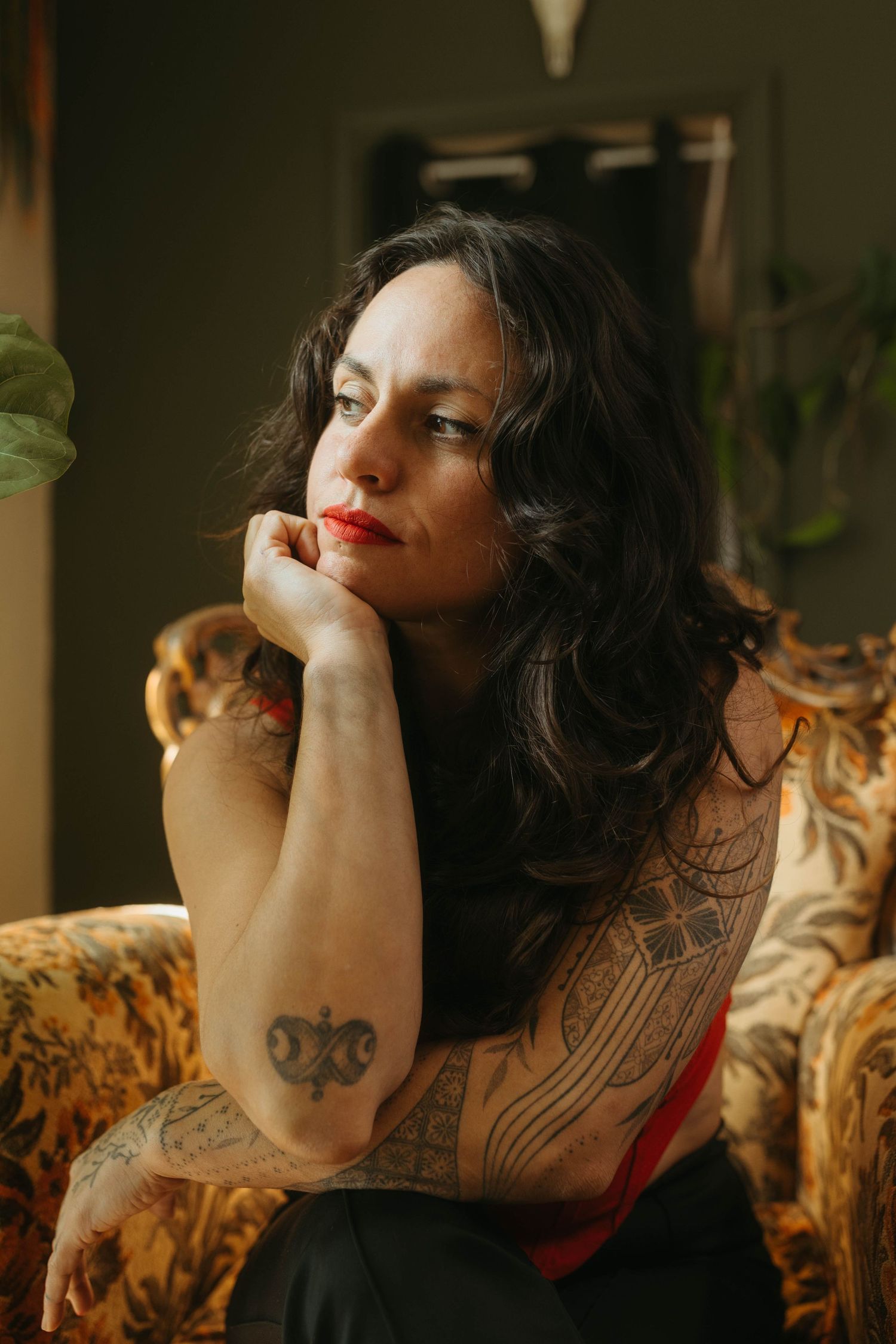 Portrait of woman leaning her chin against her hand looking to the left, dark hair and tattoos