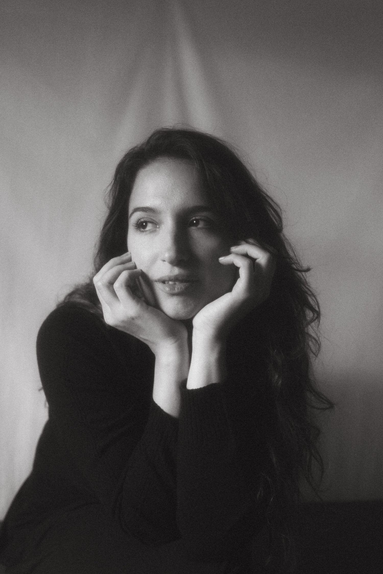 Black and white soft photograph of model in front of a white backdrop leaning against her hands