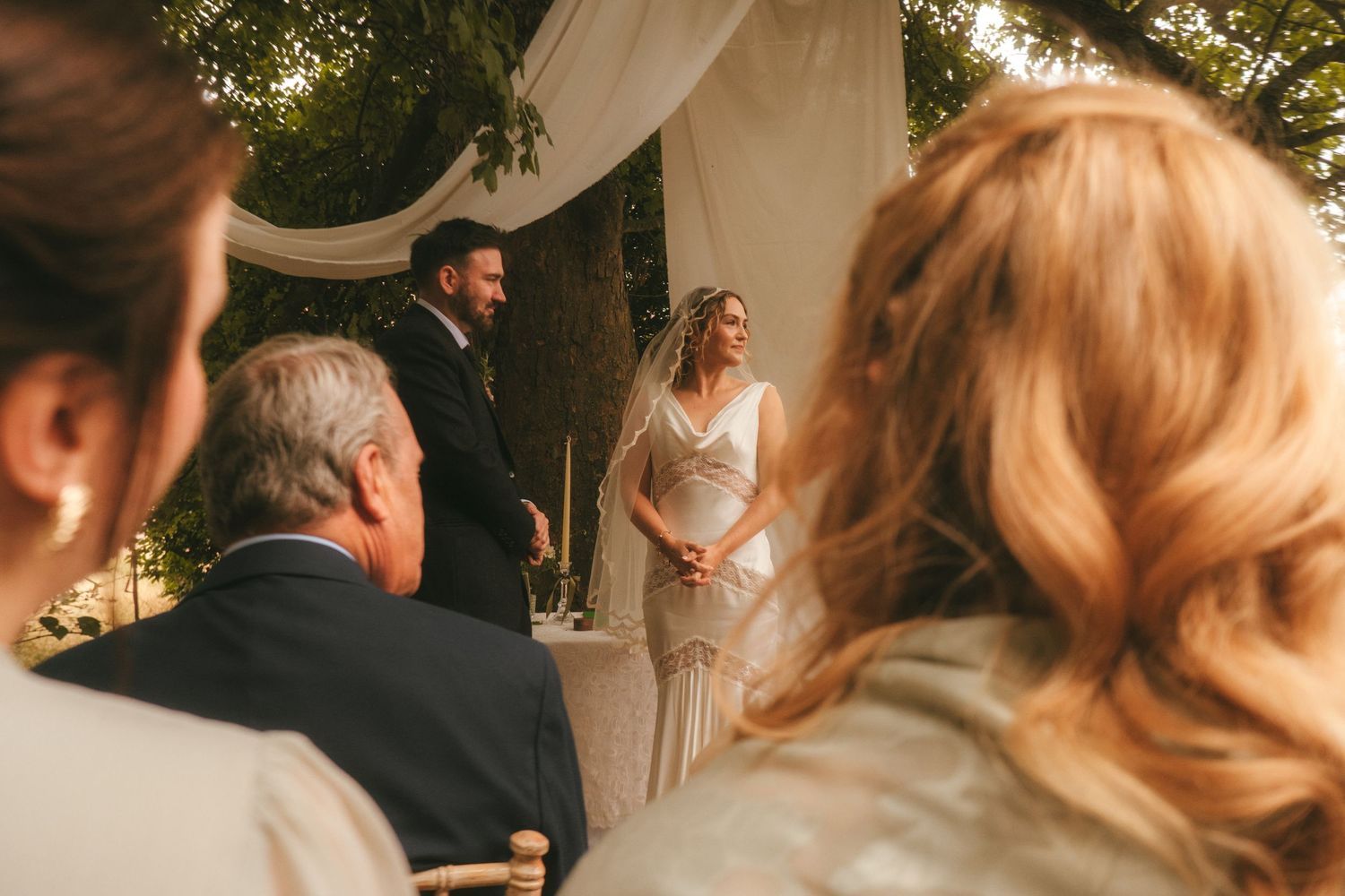Photograph of bride and groom shot from the back peeking through their guests.