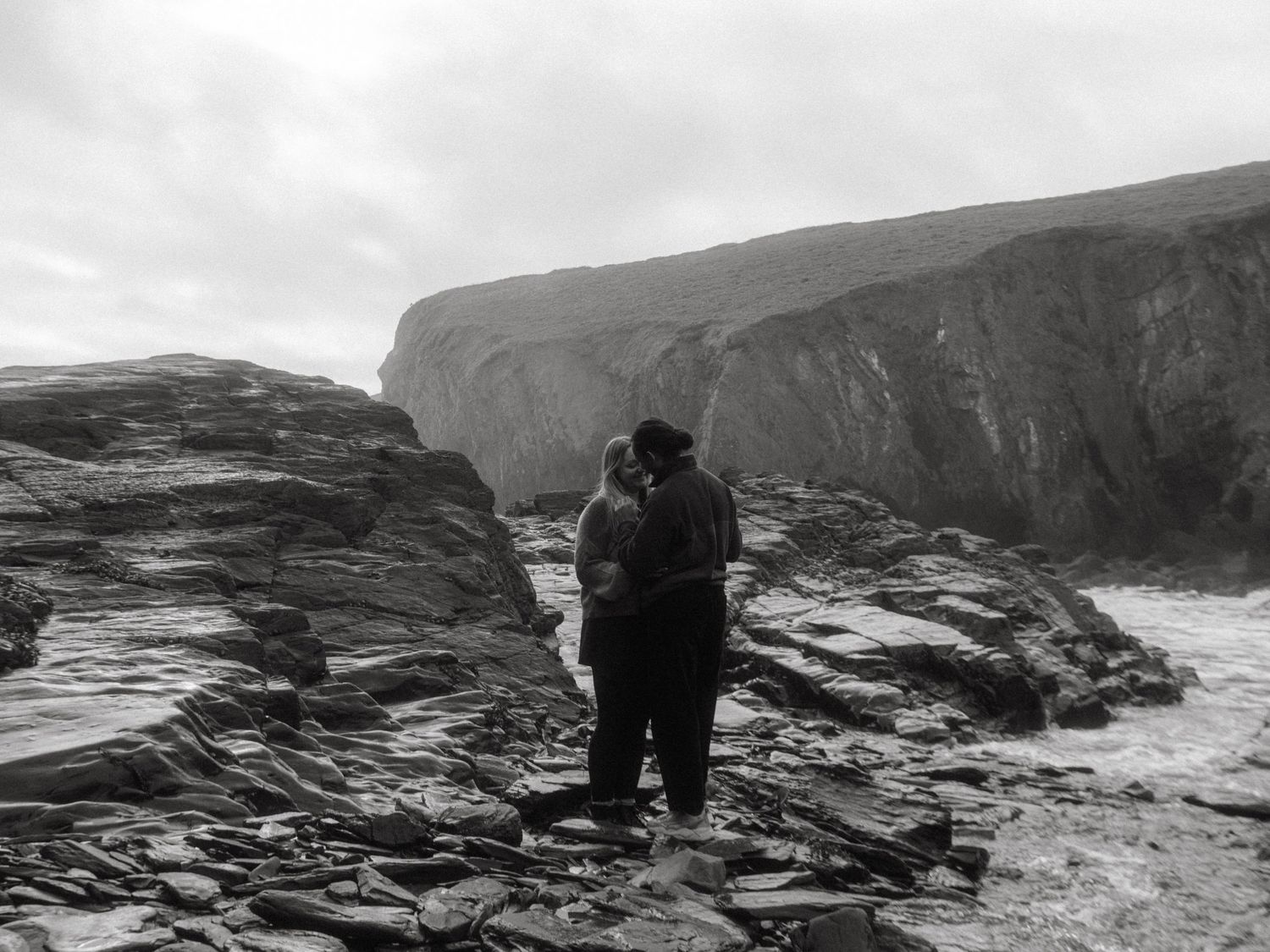 Photograph of couple posing at Nohoval Cove in Cork, Ireland. Soft contrast, warm colors.