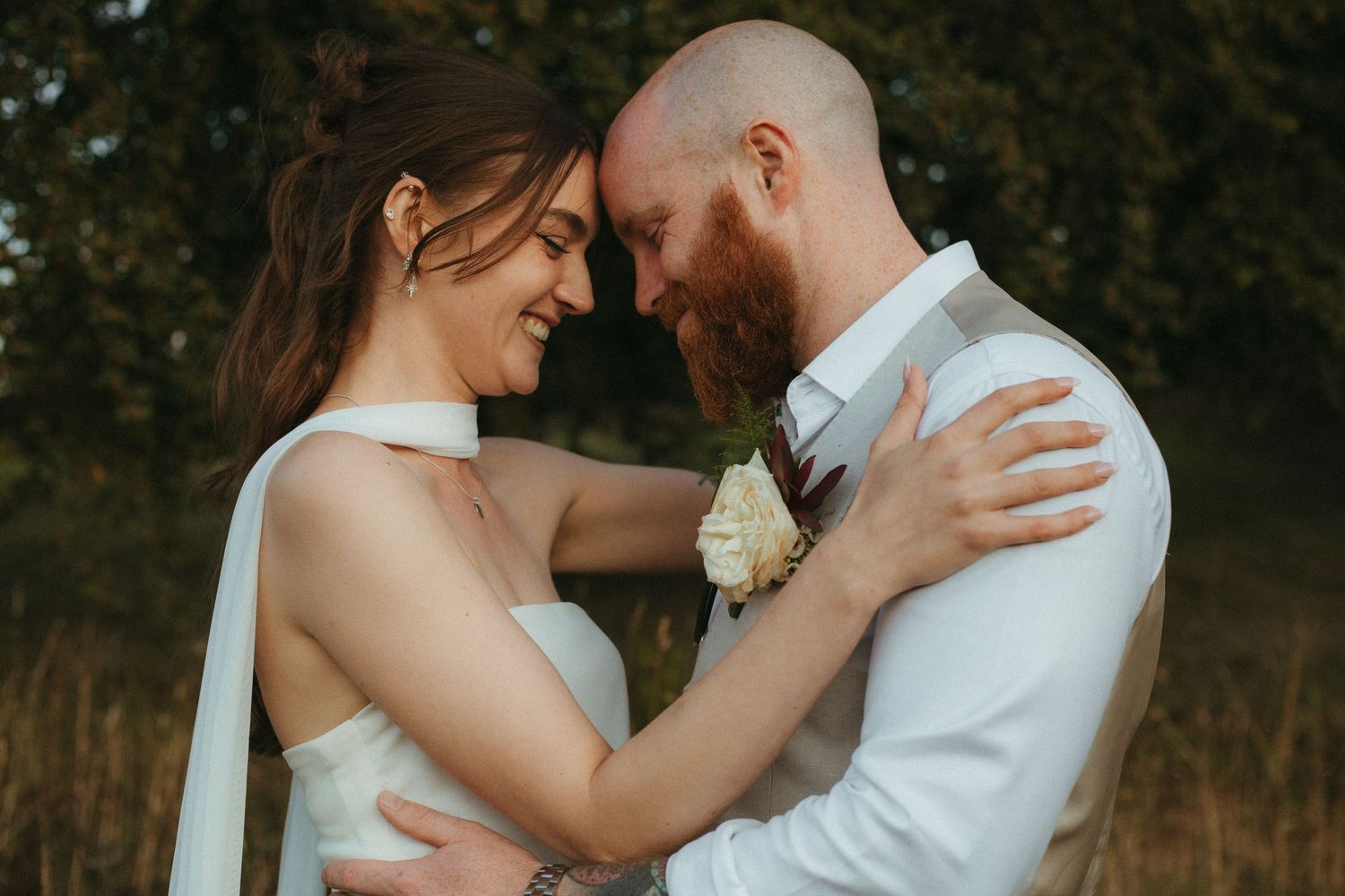 Photograph of bride and groom, she has dark brown hair and he is bald with a ginger beard.