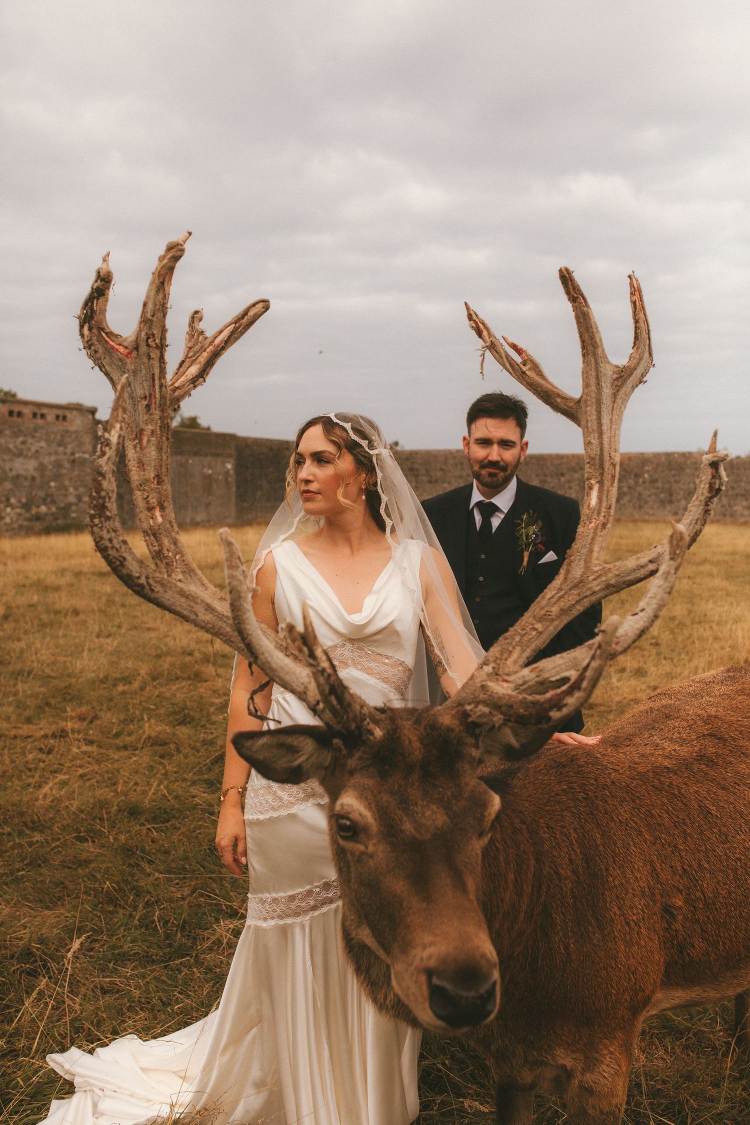 Photograph of bride and groom behind a stag. they are in focus in between the stags antlers