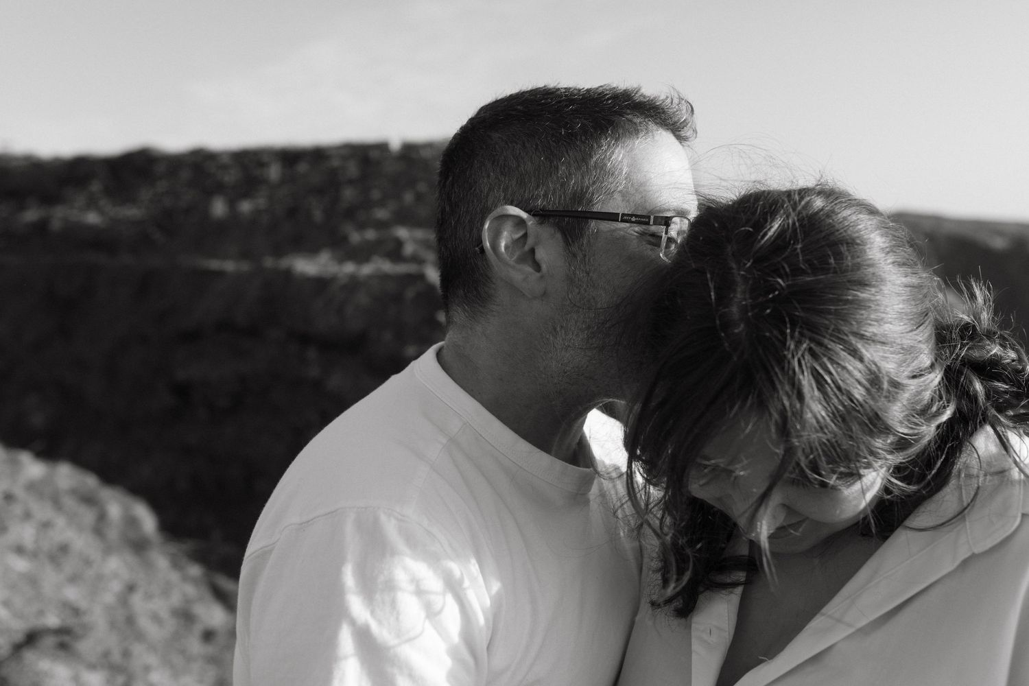 Black and white photo of a couple, he's kissing her head, you can see cliffs in the back