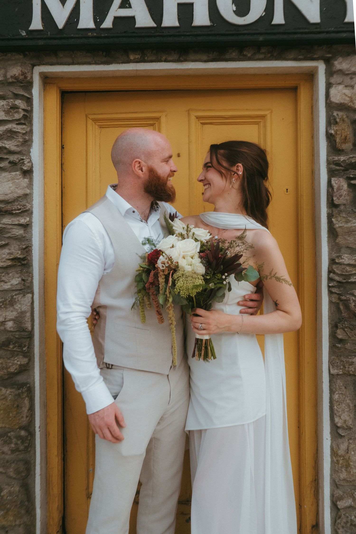 Photograph of bride and groom, she has dark brown hair and he is bald with a ginger beard.