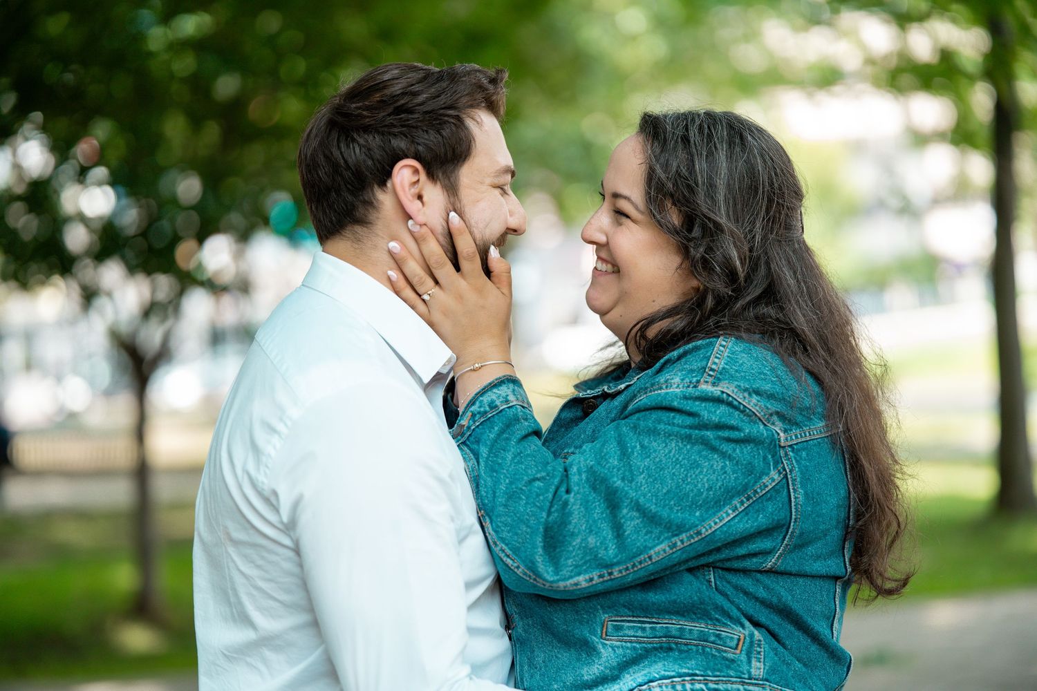 Loving couple face to face in a park, woman gently holding mans face while smiling joyfully.
