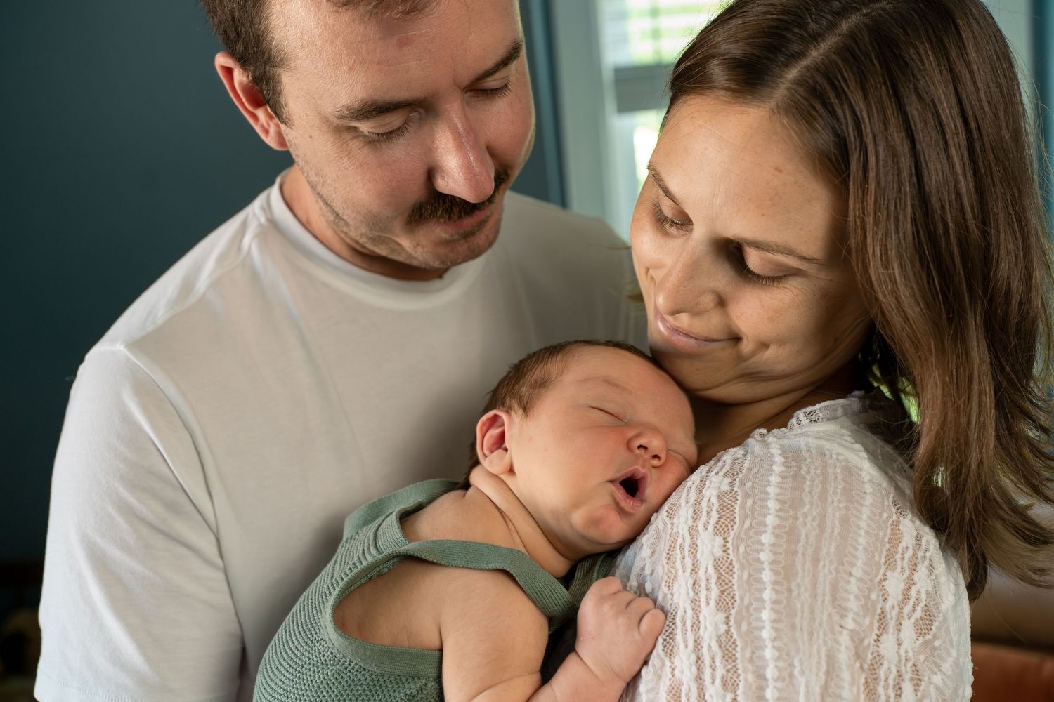 New parents tenderly holding their sleeping newborn baby during an indoor lifestyle newborn session.
