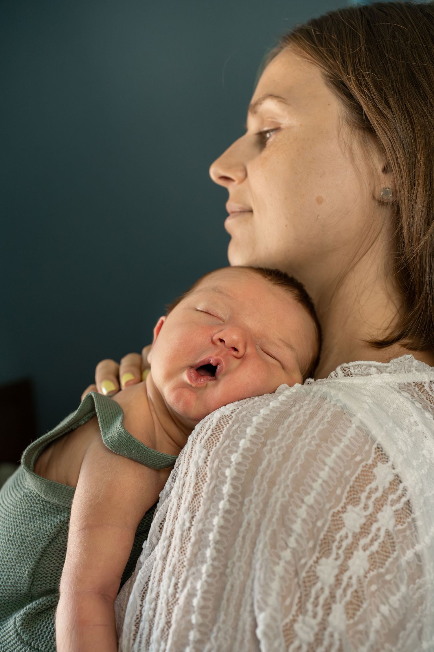 Mother holding sleeping newborn baby on her shoulder in a tender and peaceful indoor portrait.