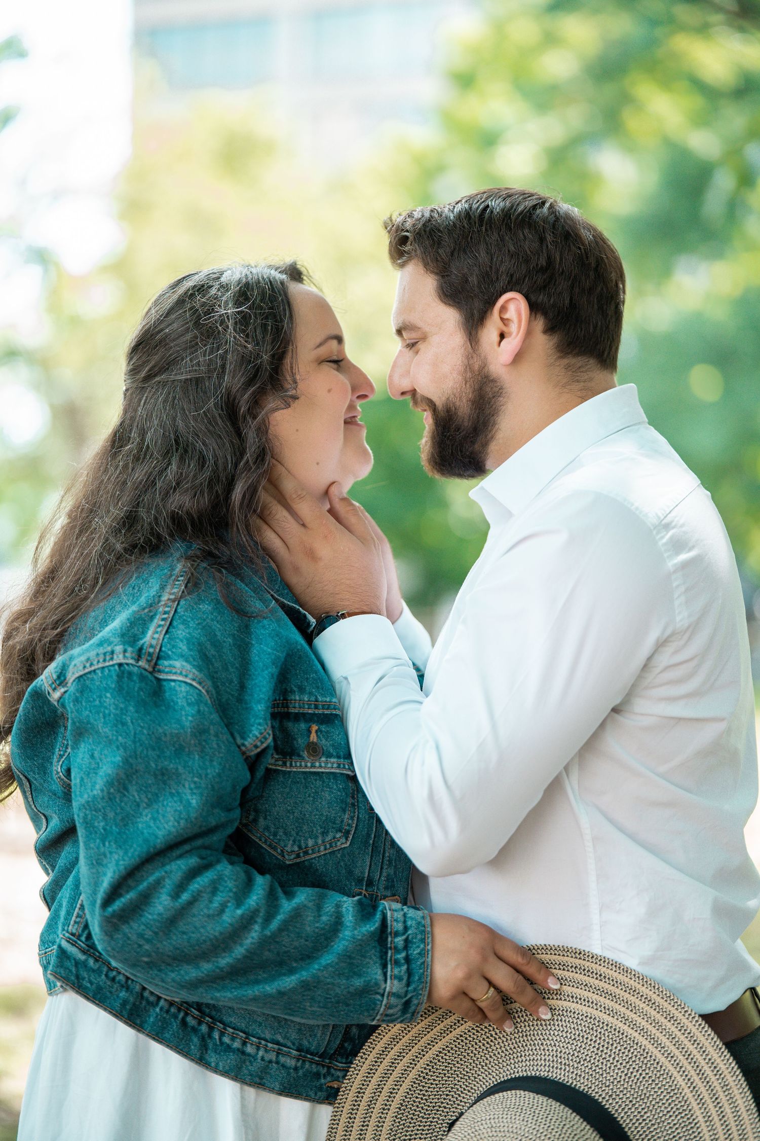 A bearded man tenderly cups a woman's face as they lean in for a kiss outdoors.