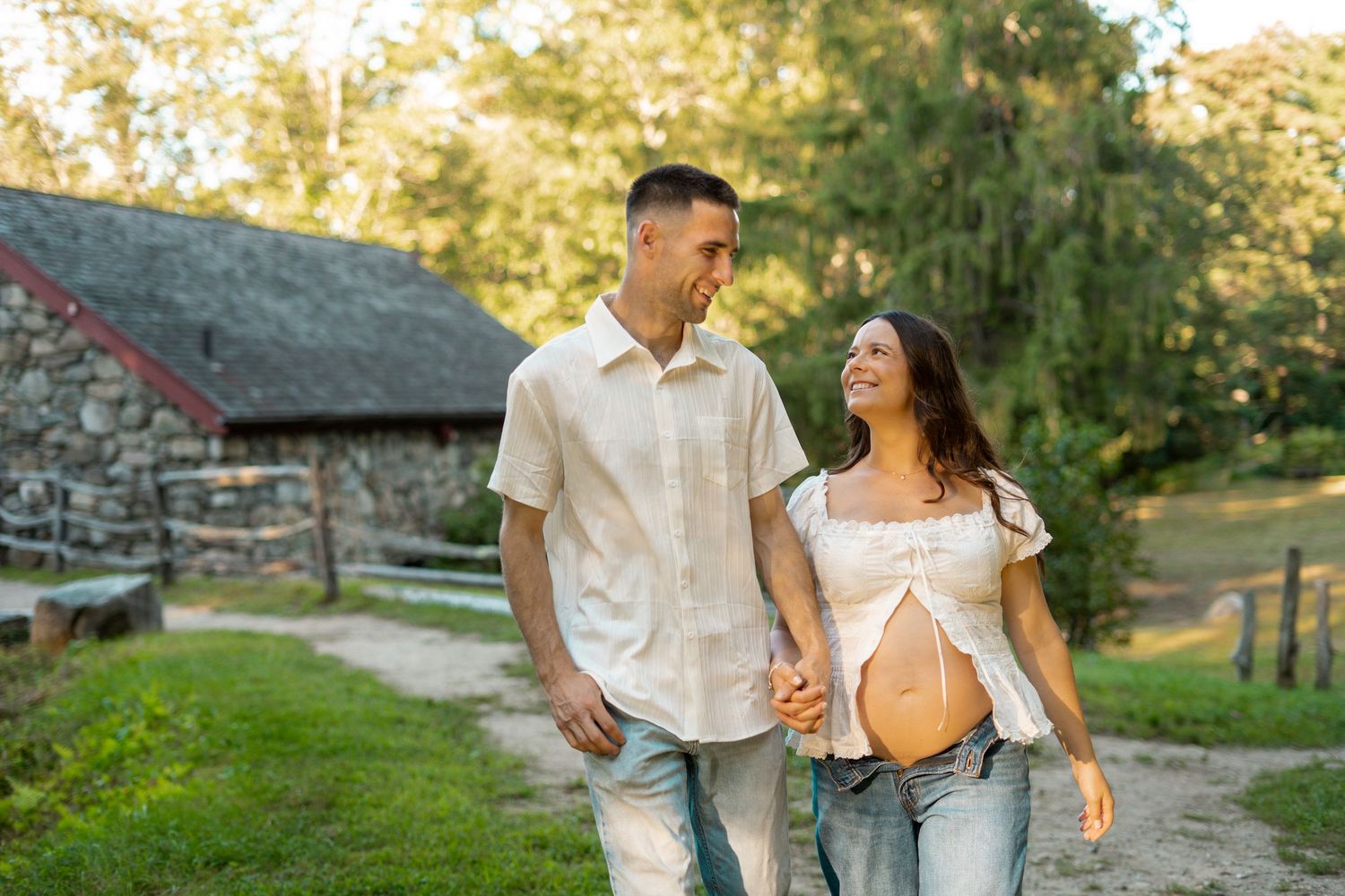 A couple walks towards the camera, he is starting at her. She is pregnant and staring at him. Longfellow Wayside Inn Grist Mill building.
