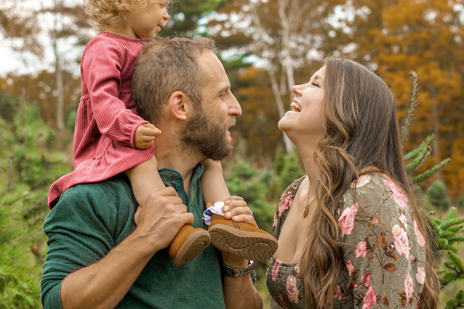 Joyful family with a toddler on dad's shoulders sharing a laugh in an autumn forest.