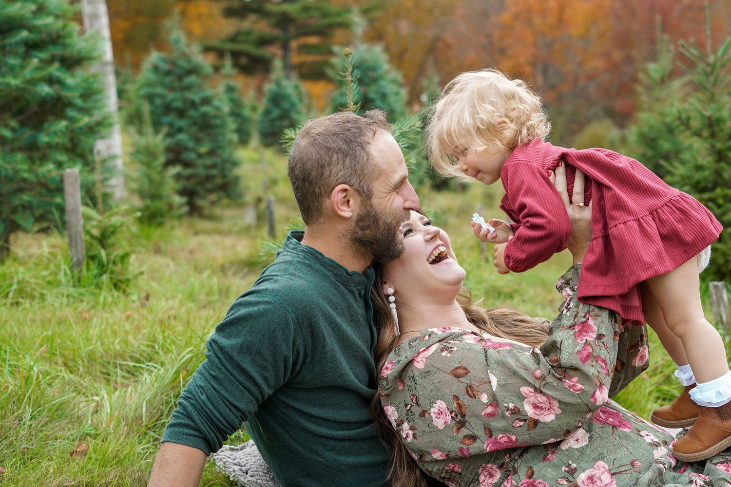 Joyful family of three playing together in a grassy field near evergreen trees during autumn season.