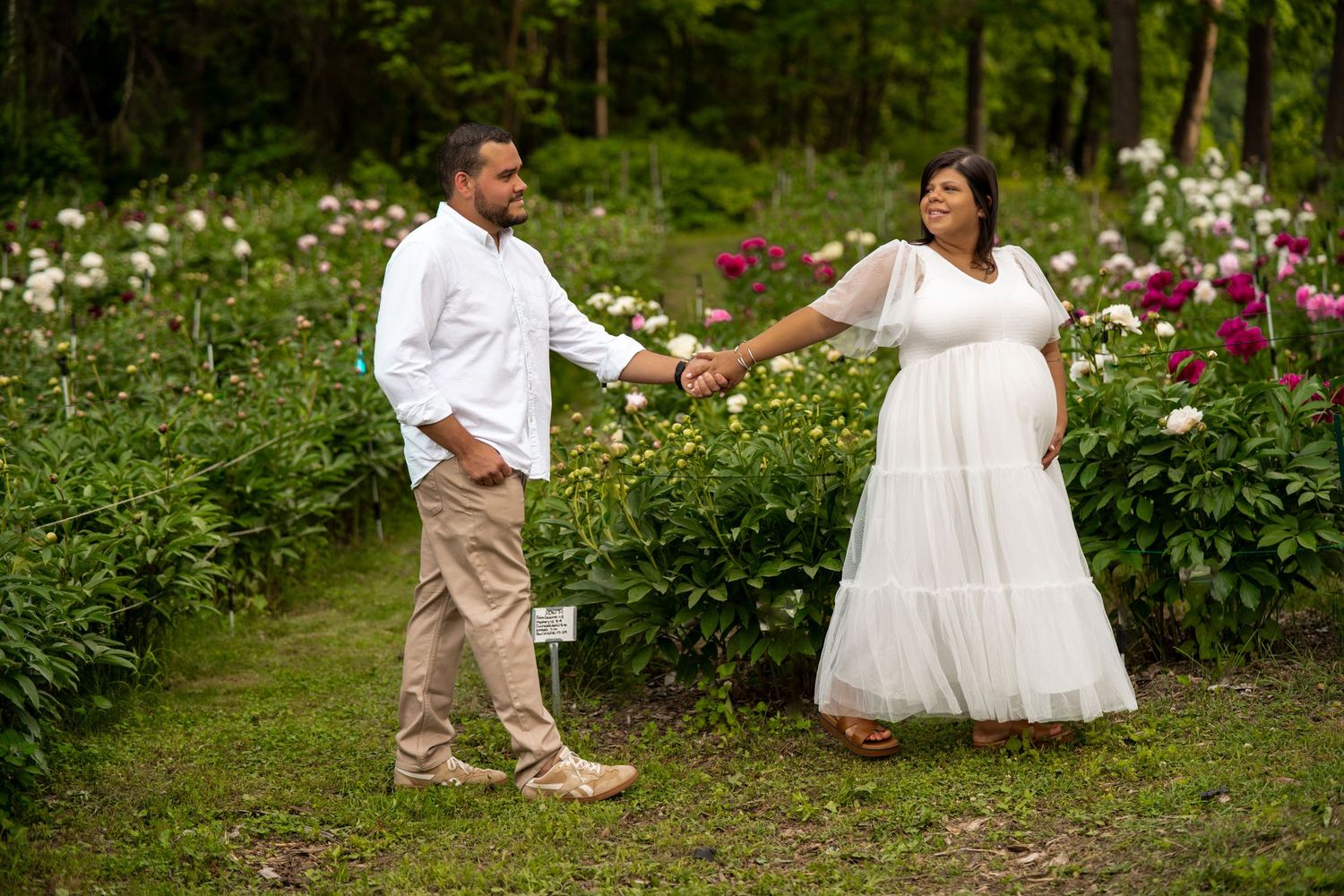 Expecting couple holding hands and walking through a lush garden during a maternity photo session.