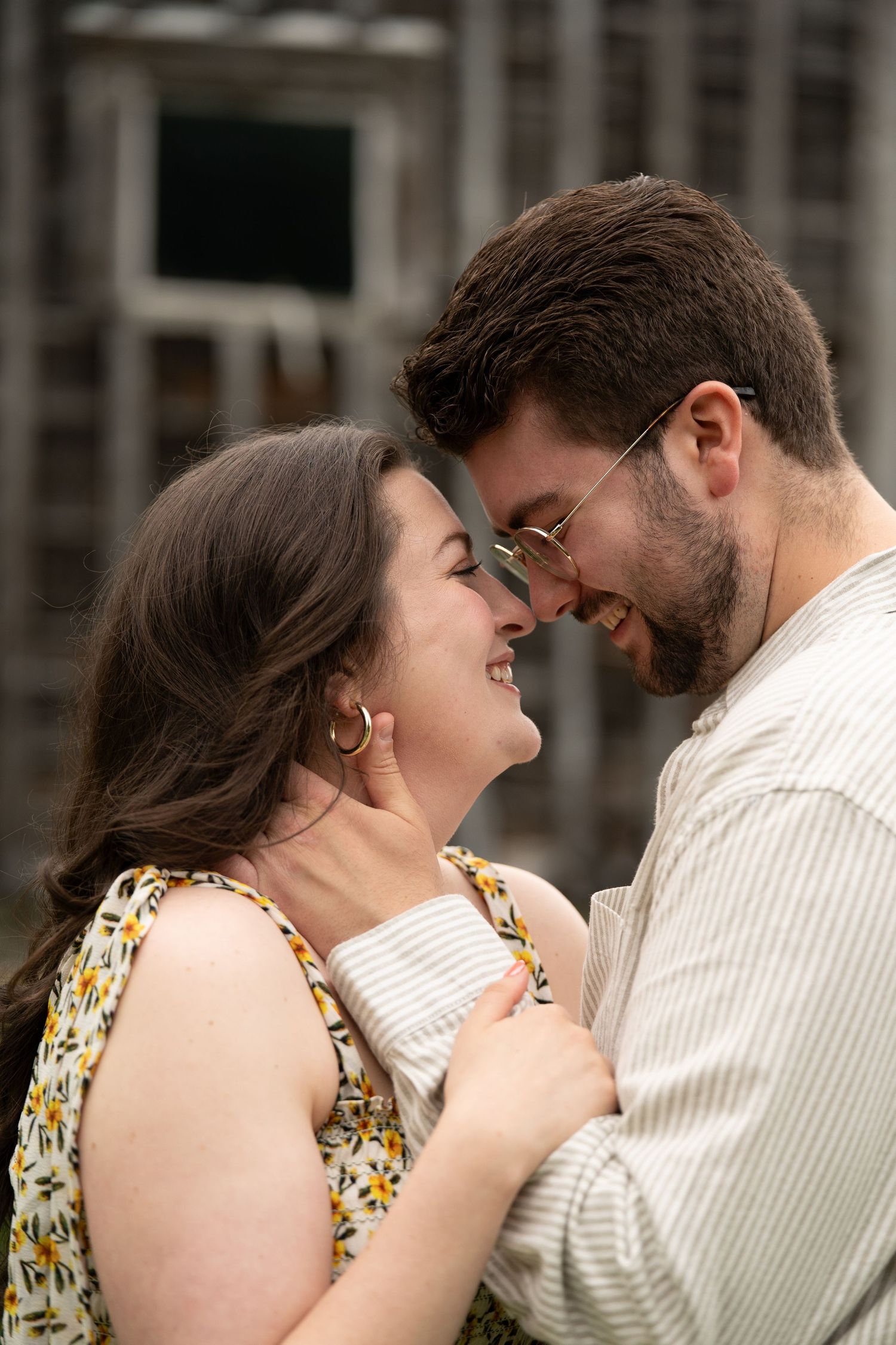 Couple smiling and touching foreheads in a romantic moment, woman in floral dress, man with glasses.