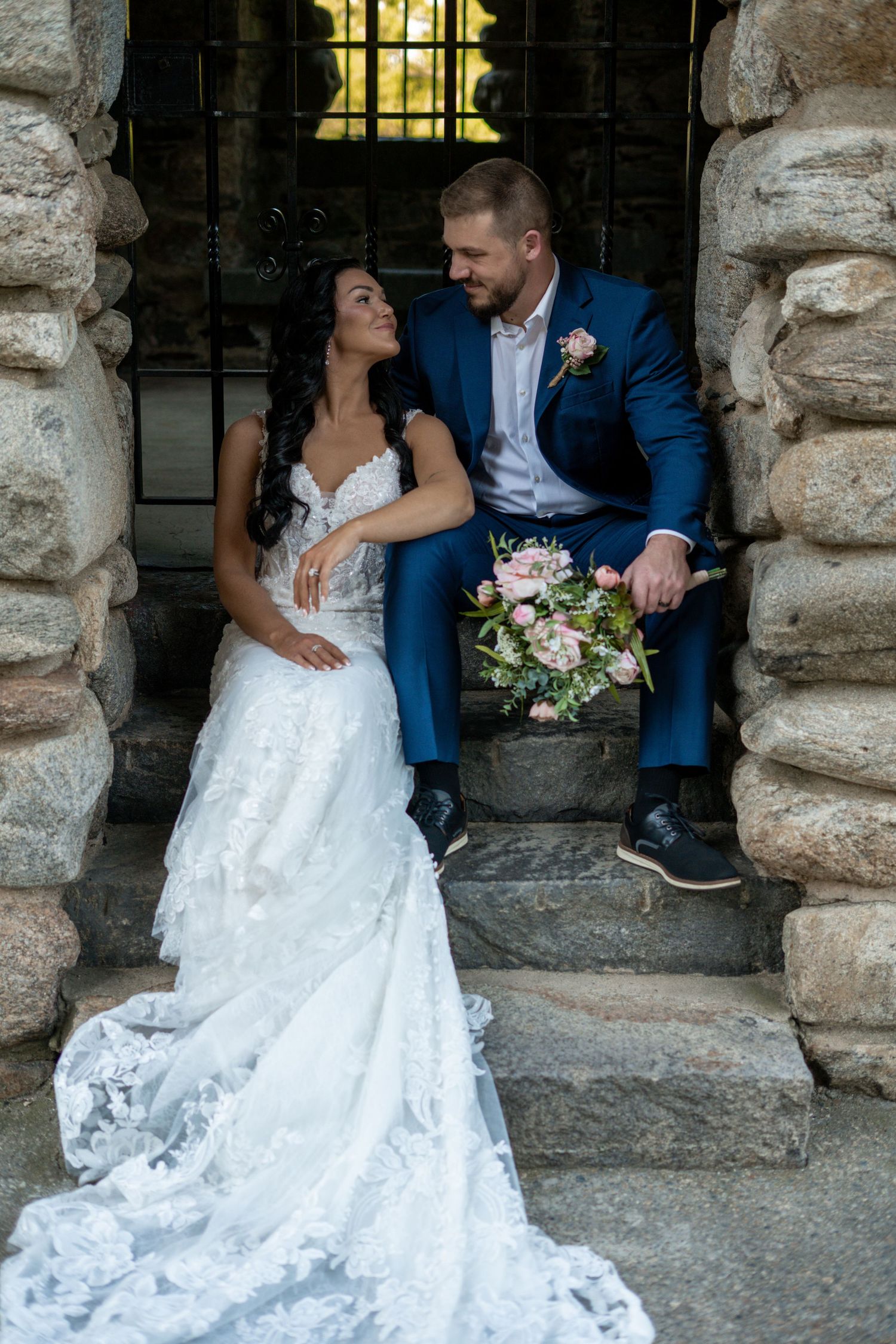 Bride and groom sharing a tender moment on stone steps of a rustic castle venue.