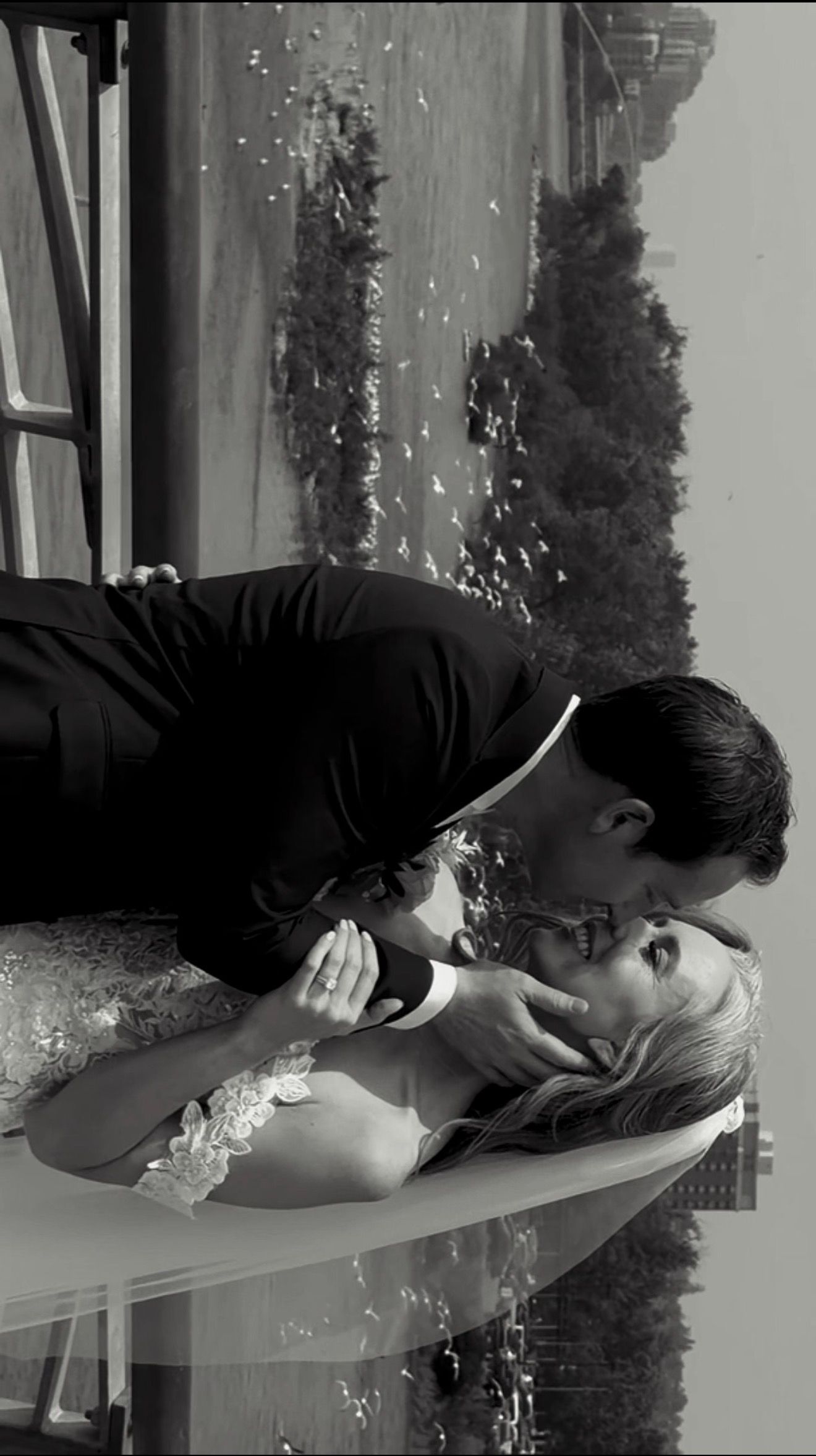 Black and white romantic photo of groom dipping and kissing bride in wedding attire.