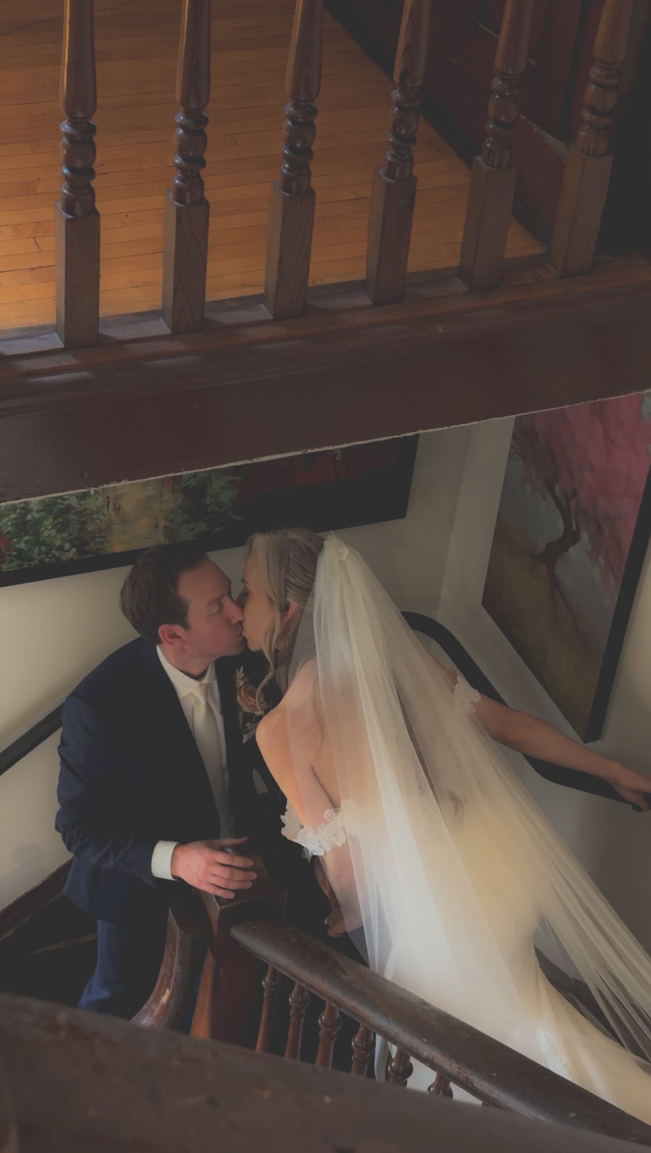 Bride and groom share tender kiss on wooden staircase, brides veil cascading elegantly.
